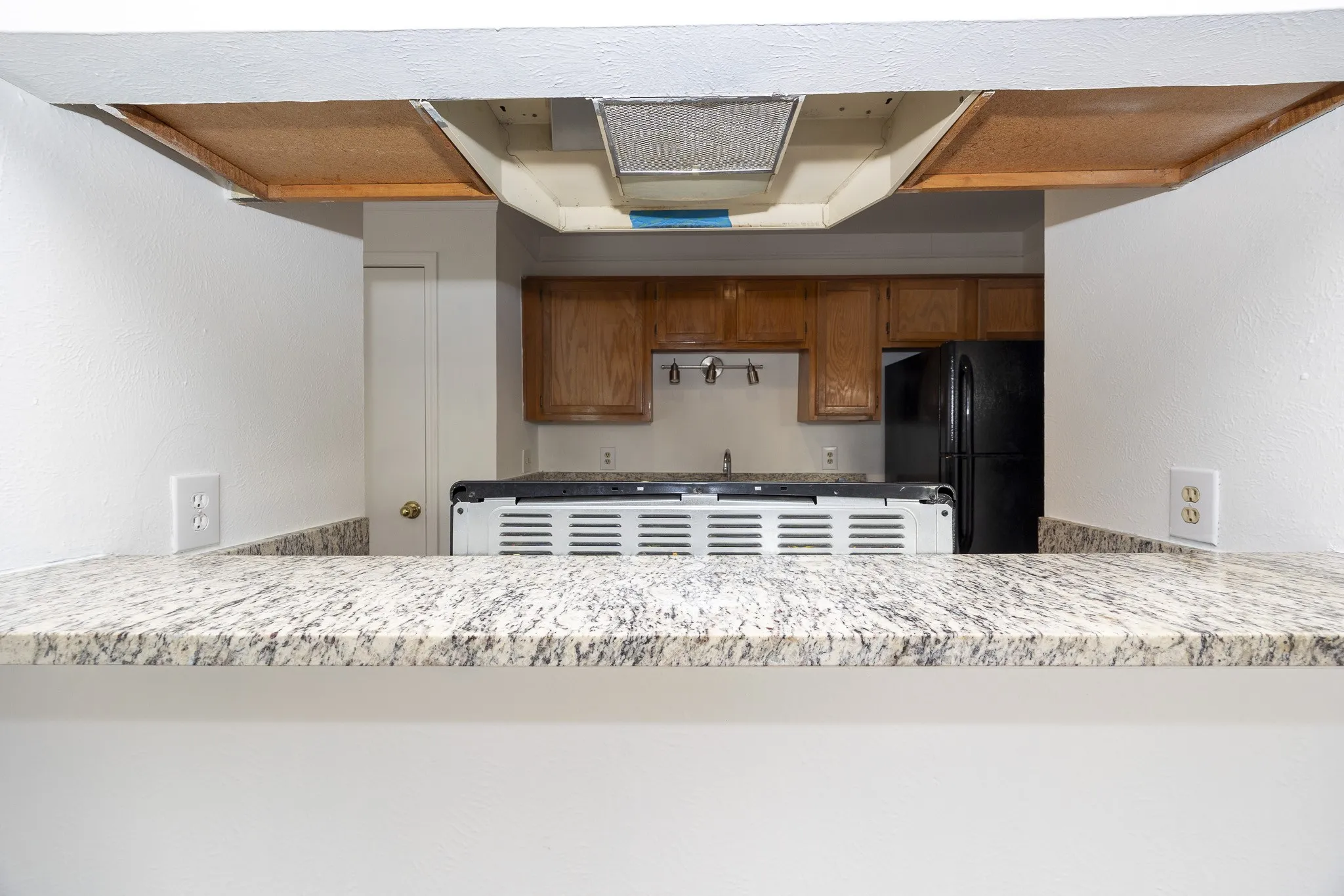 Modern kitchen showcasing a granite-style countertop with waterfall edge, white cabinetry with stainless steel hardware, stainless steel appliances including a black refrigerator, gas cooktop, and range hood, with recessed lighting and wood-finish ceiling accents