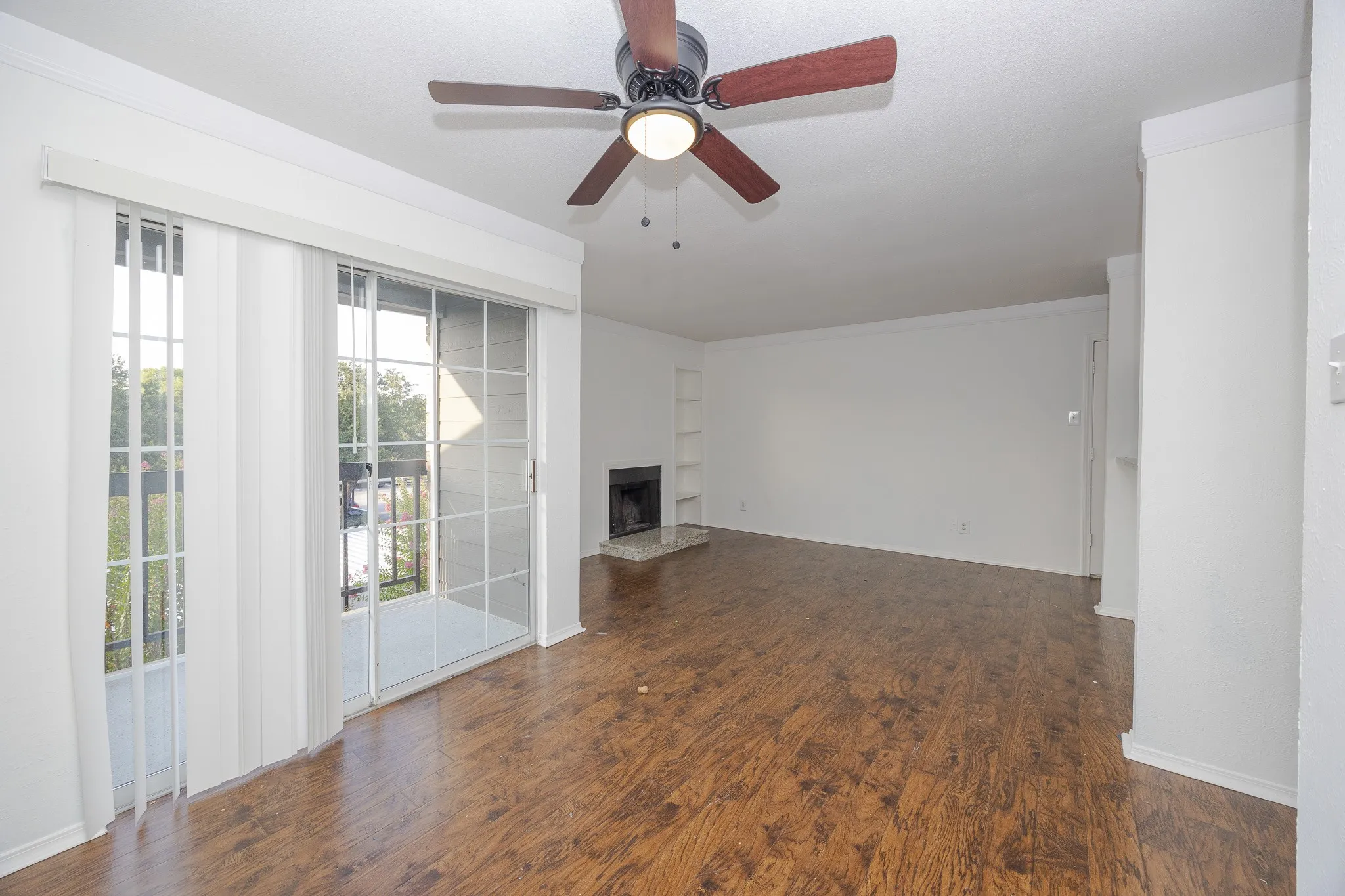 Spacious living area featuring wood-finish flooring, a ceiling fan with integrated lighting, and a fireplace with a hearth