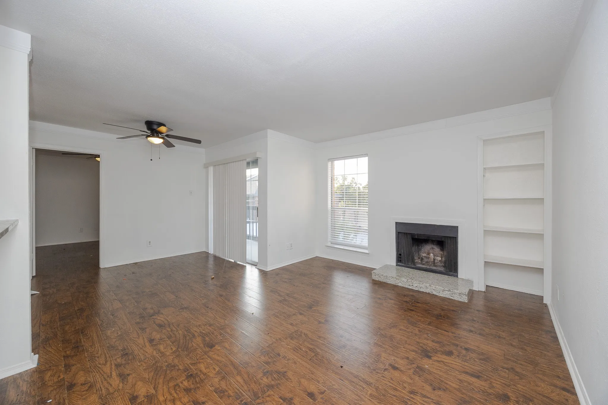 Wood-finish flooring, built-in shelving, fireplace with stone hearth, sliding glass door, and ceiling fan