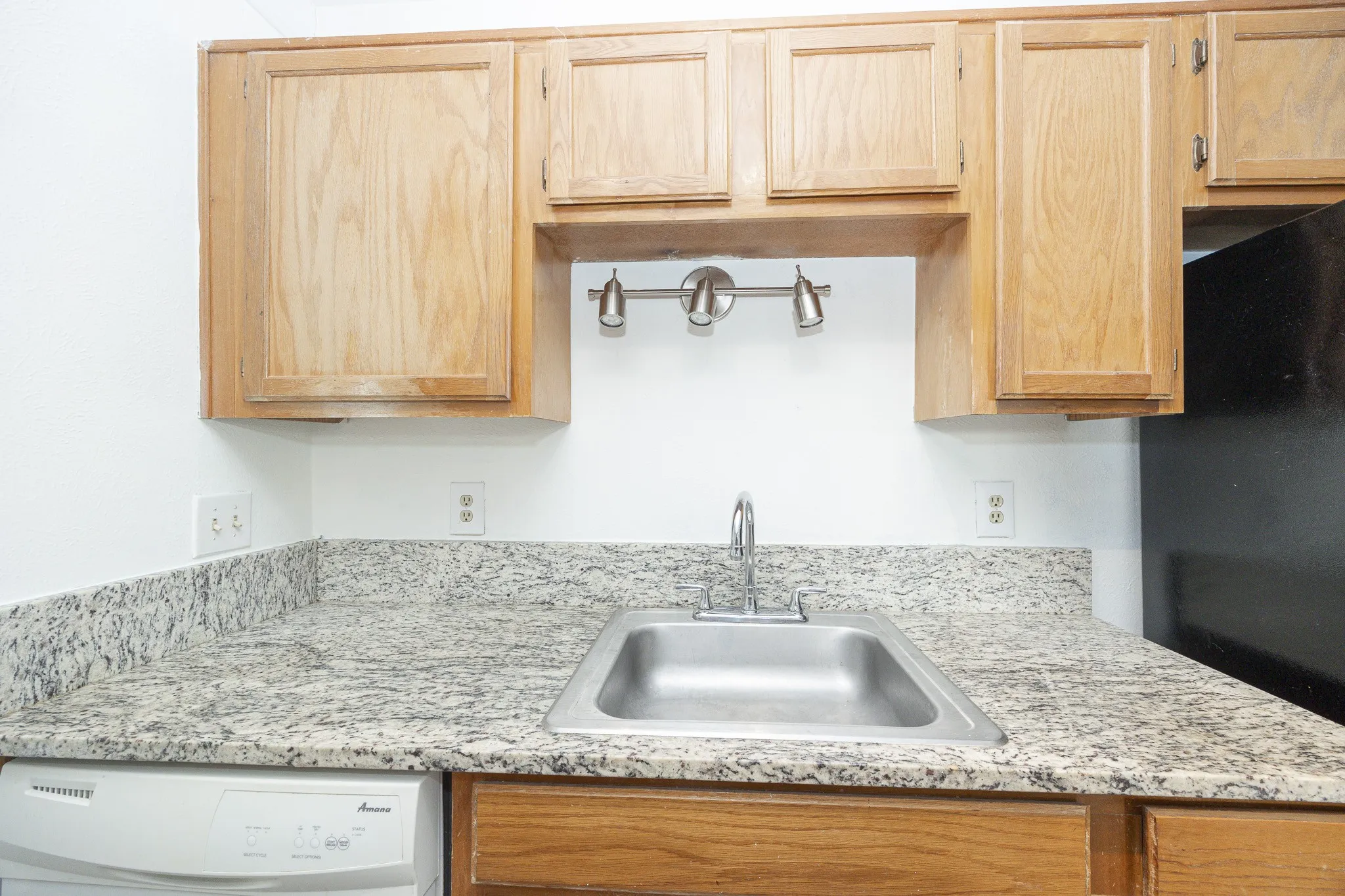 Granite-style countertops with an undermount stainless steel sink, wood cabinetry, and a full-size dishwasher