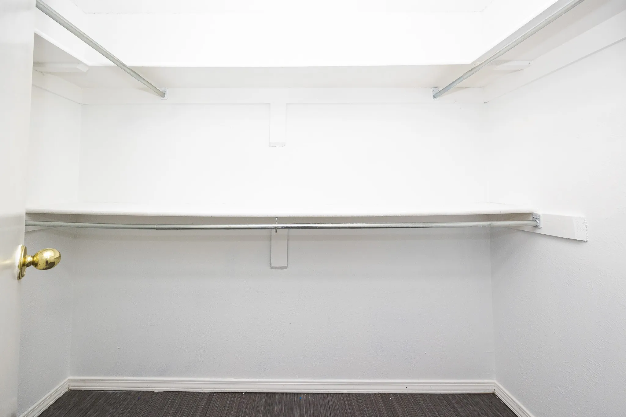 White interior with dark wood-finish flooring, featuring a brass-tone doorknob, and built-in shelving with hanging rods