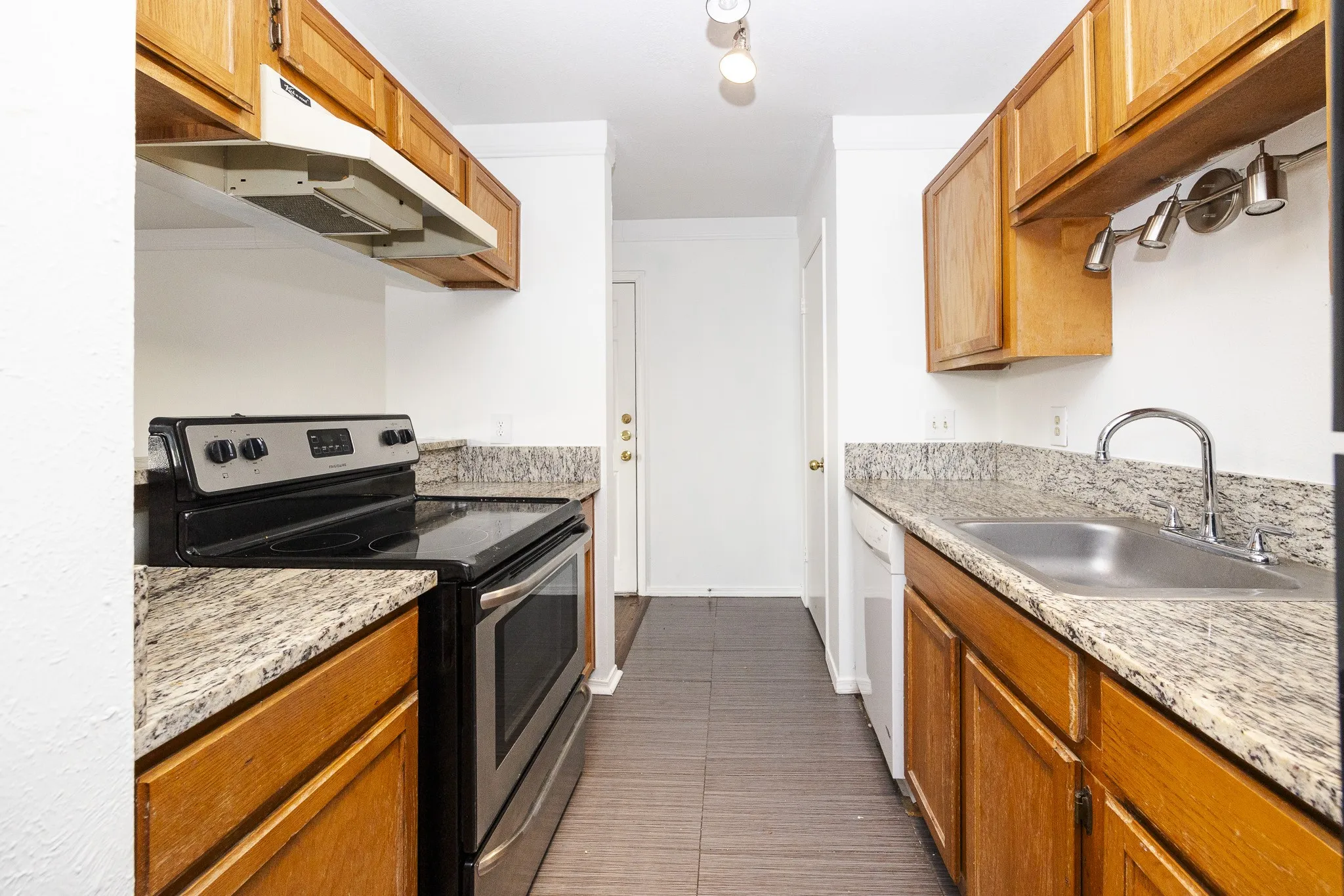 Galley kitchen featuring wood cabinetry, granite-finish countertops, stainless steel appliances, a stainless steel sink, and tile flooring