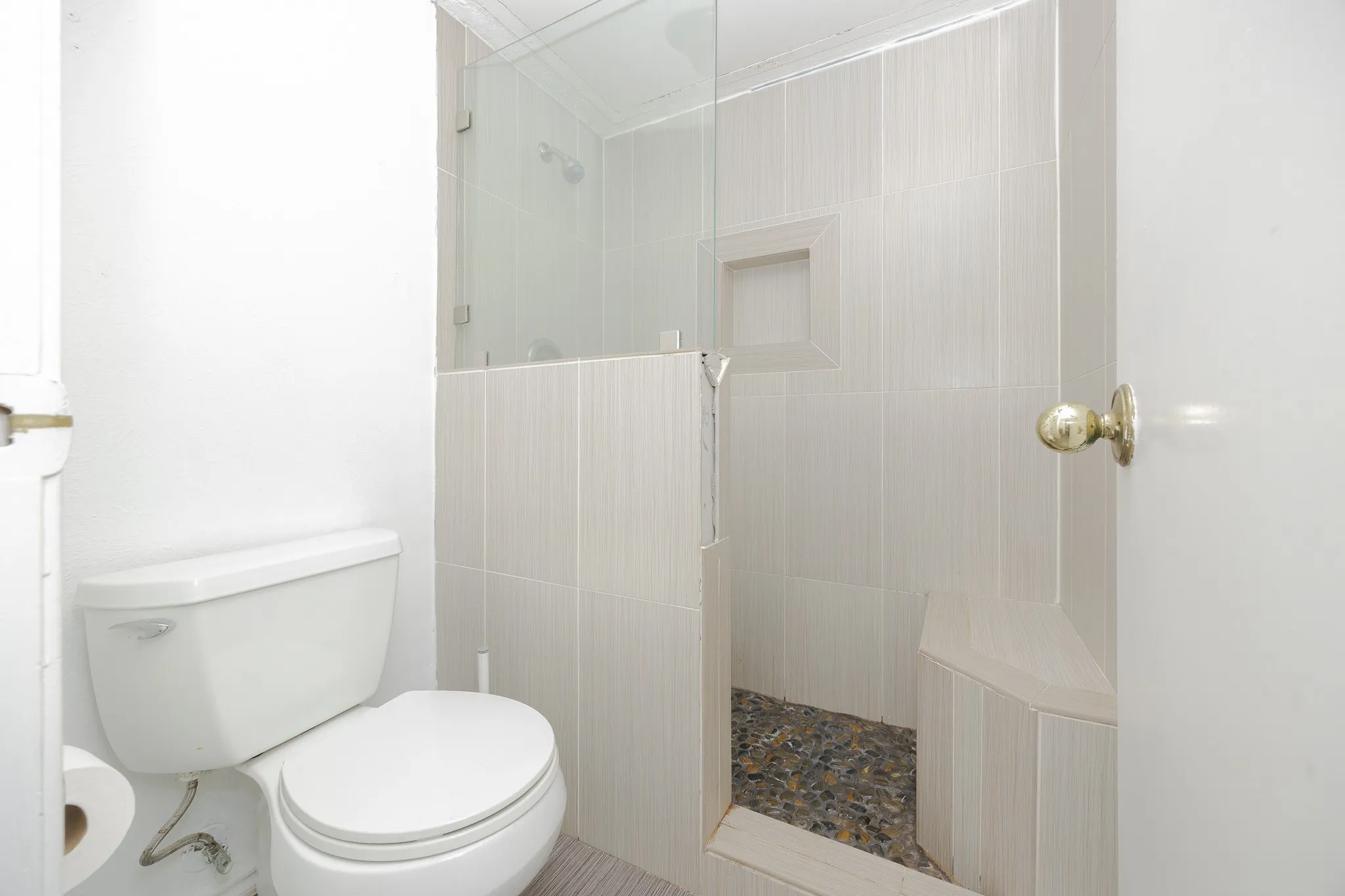 Glass-enclosed shower with a built-in bench, tiled walls, and a pebble-finish floor