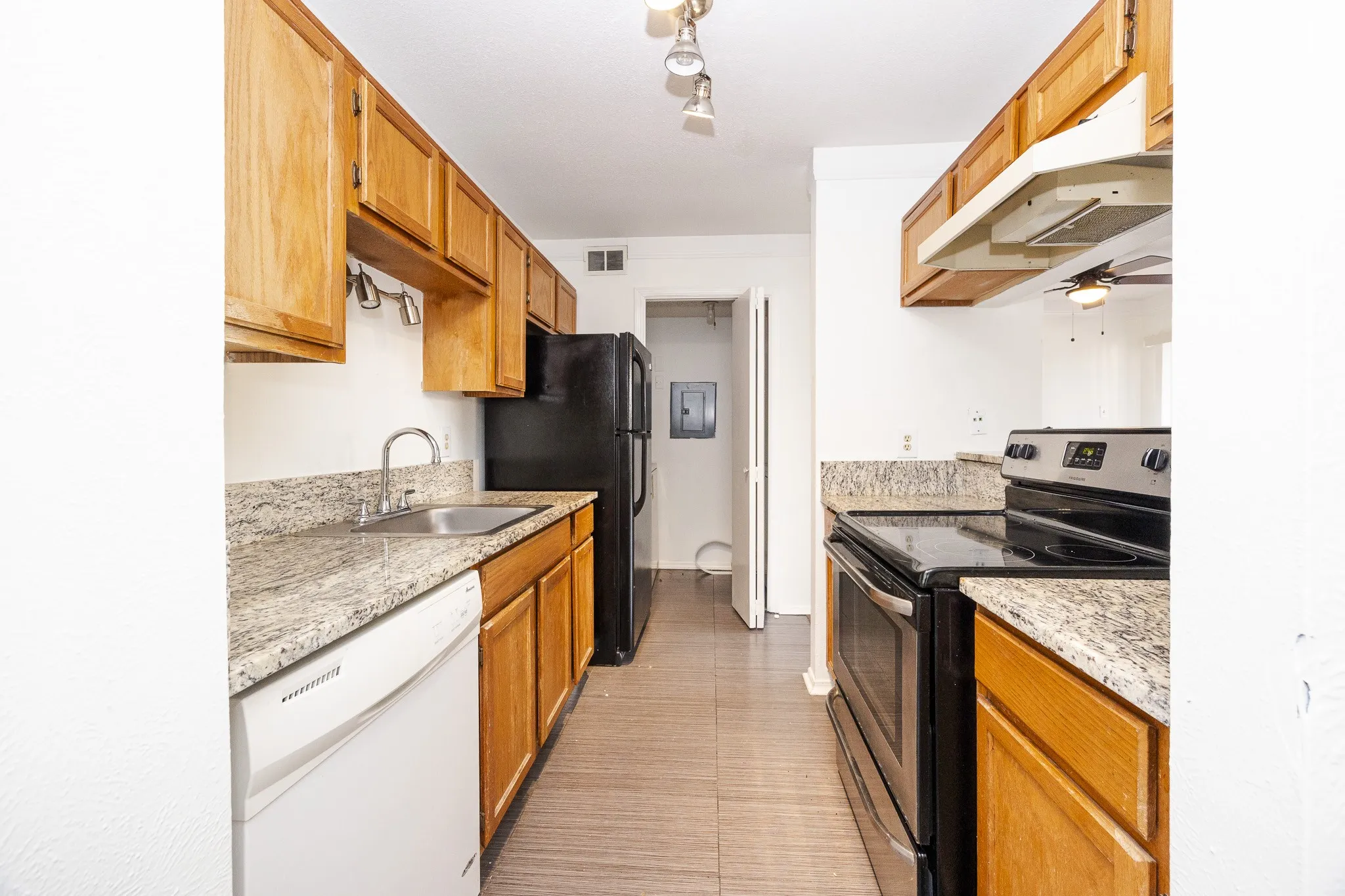 Kitchen featuring wood cabinetry, granite-style countertops, stainless steel sink, black range, and black refrigerator