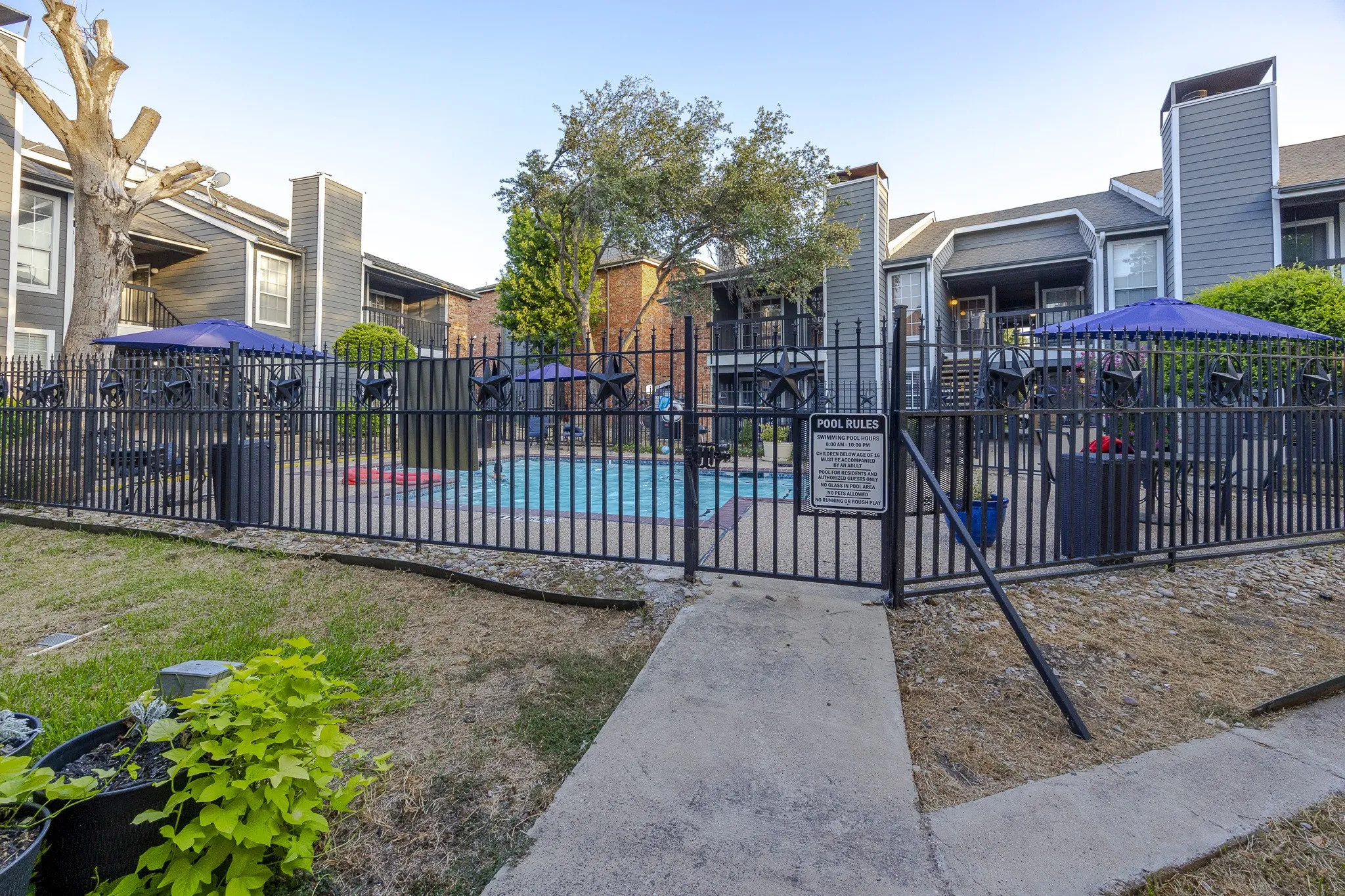 Fenced swimming pool area with concrete decking, surrounded by apartment buildings featuring balconies and dark siding