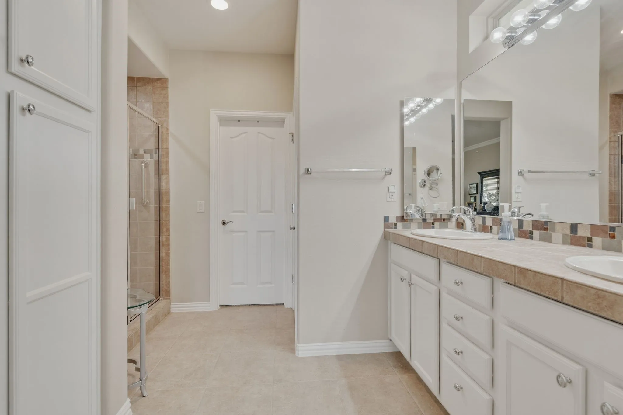 Dual vanity with white cabinetry, integrated sinks, tile countertop, and a mosaic tile backsplash