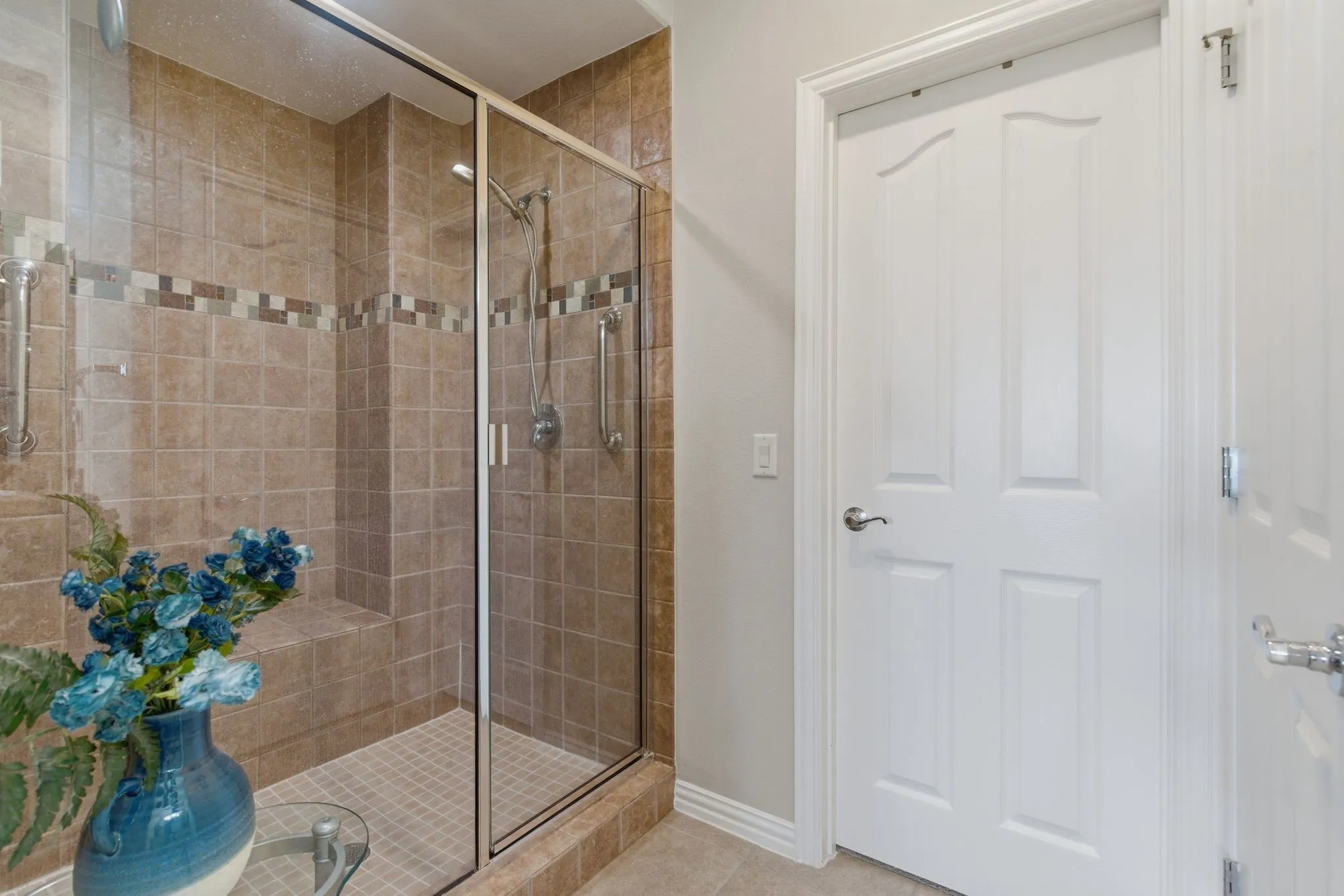 Tiled shower enclosure featuring a glass door, built-in bench, and grab bars