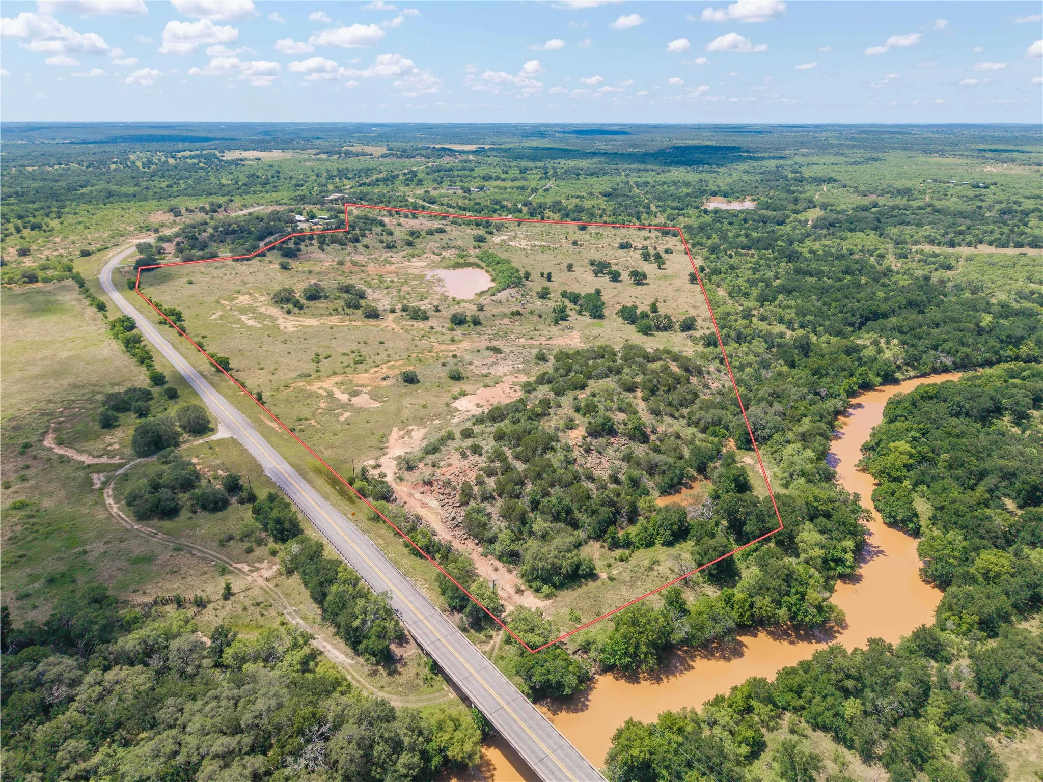 Expansive acreage featuring a winding river frontage, mature tree coverage, a visible pond, and direct road access via a bridge