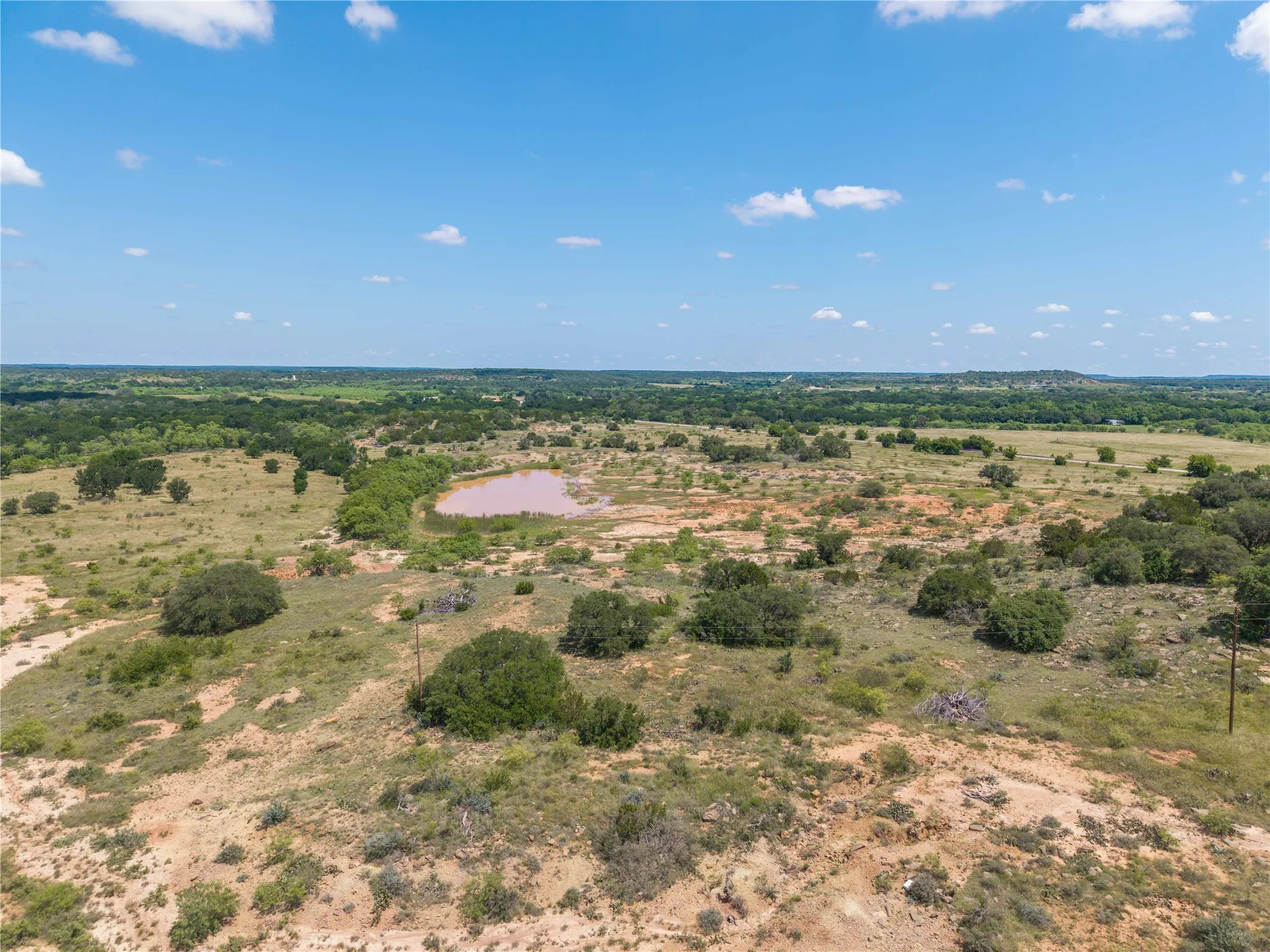 Expansive natural landscape featuring varied terrain, a large water feature, scattered native trees, and broad stretches of open land under a clear sky