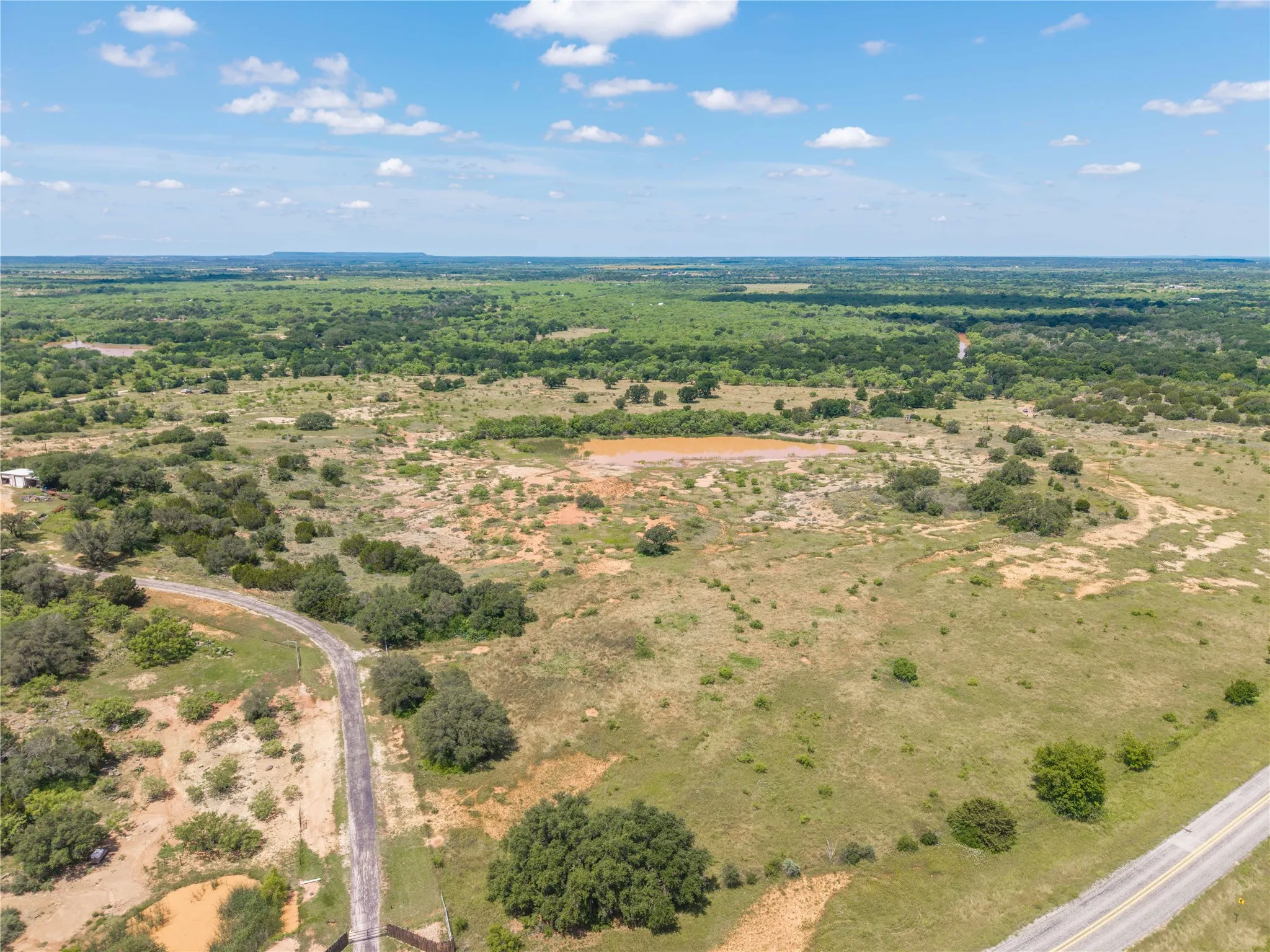 Expansive rural landscape featuring a private access road, a large pond, and diverse terrain