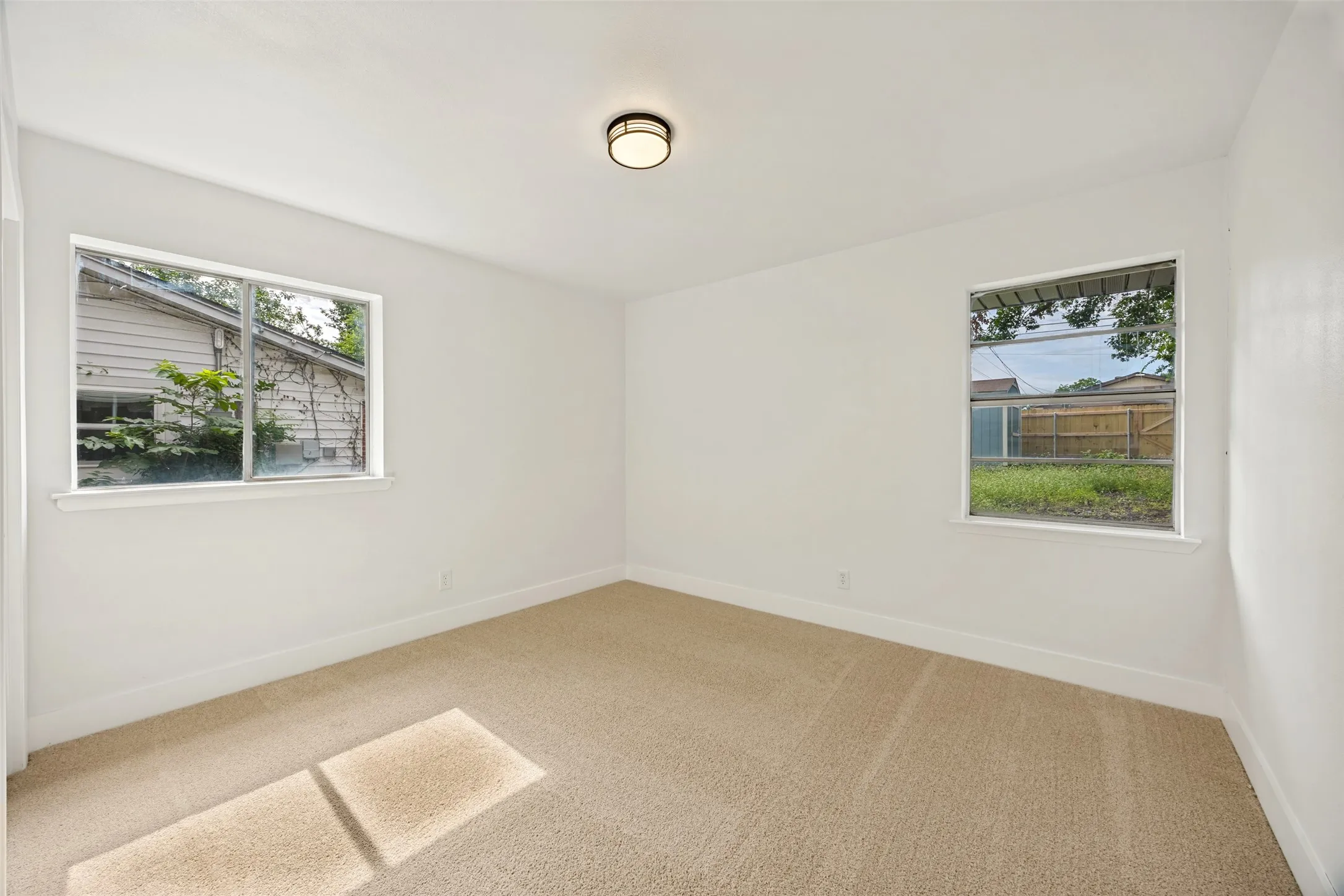 Neutral white walls with a tan carpet floor, featuring two windows and a flush-mount ceiling light fixture