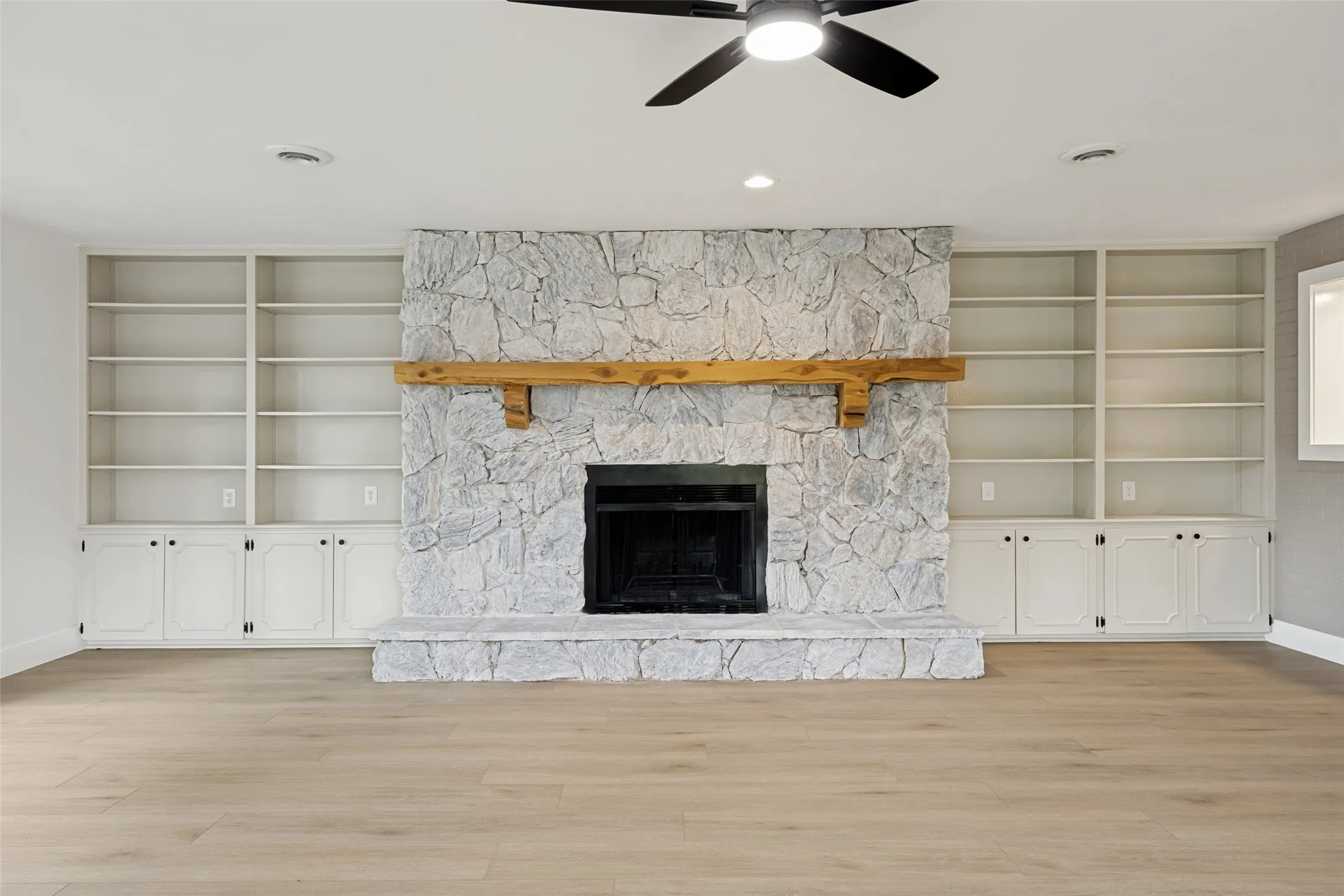 Stone-clad fireplace with a wood mantel, flanked by built-in white cabinetry and open shelving