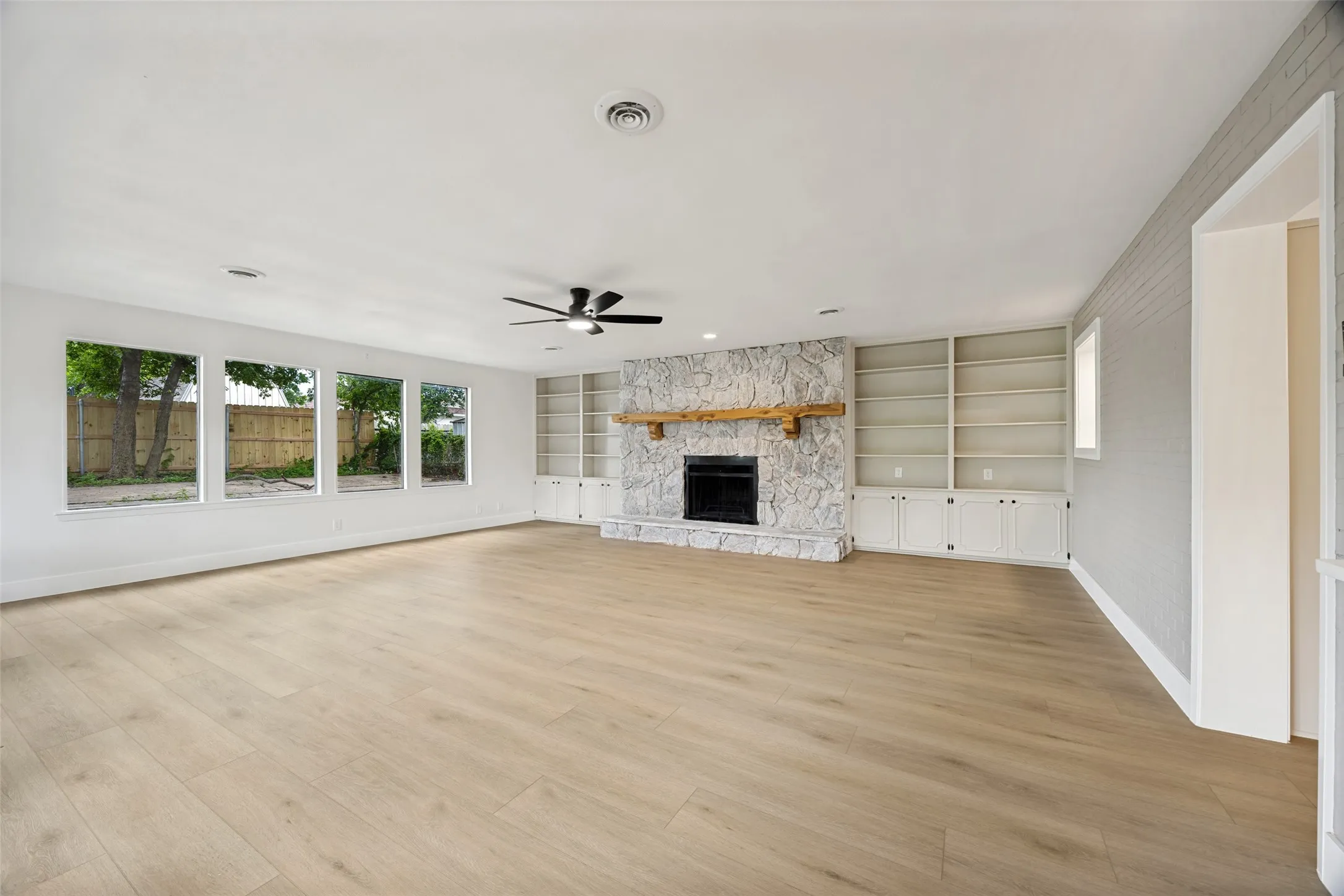 Spacious living area featuring light wood-finish flooring, a stone-clad fireplace with a wood mantle, and built-in shelving with cabinetry