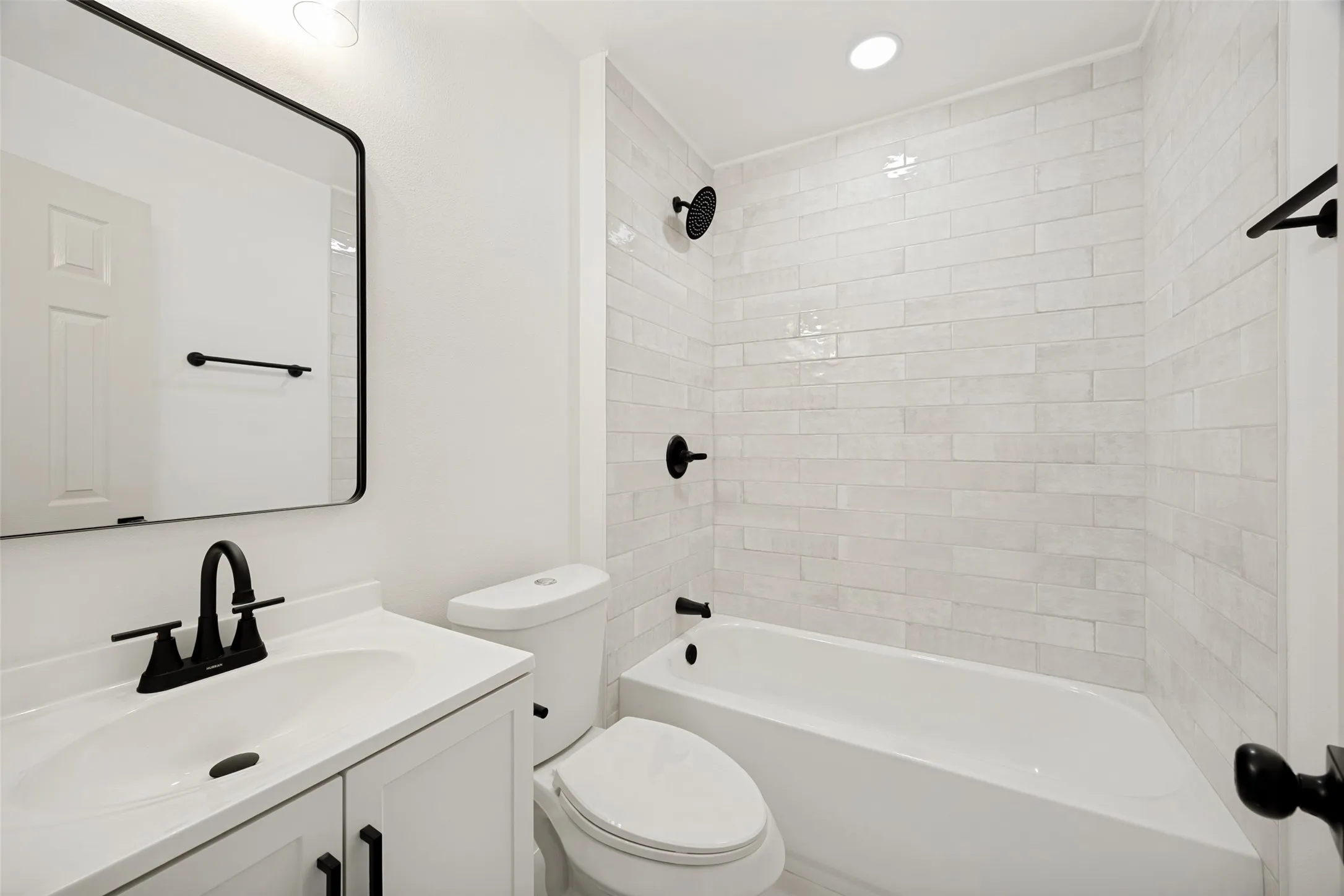 Bathroom featuring a white subway tile shower surround, matte black fixtures, a white vanity with a matching countertop, and an oval-framed mirror