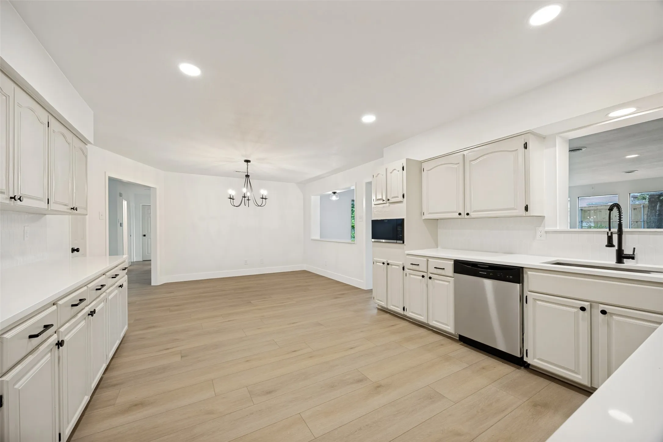 Open-concept kitchen and dining area featuring white cabinetry, light wood-finish flooring, recessed lighting, and a modern chandelier