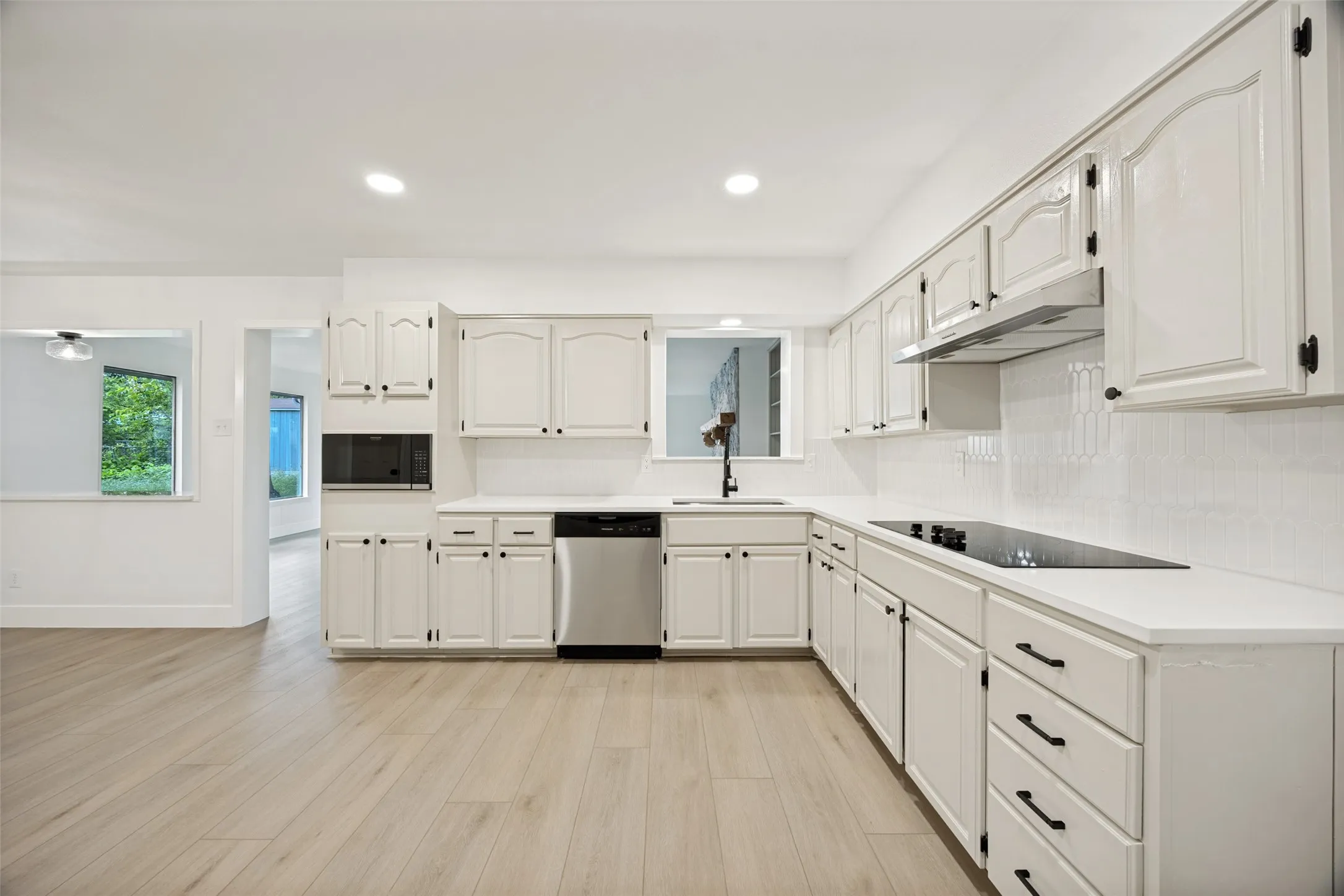 Spacious kitchen featuring white cabinetry, light countertops, wood-finish flooring, a stainless steel dishwasher, and a built-in microwave