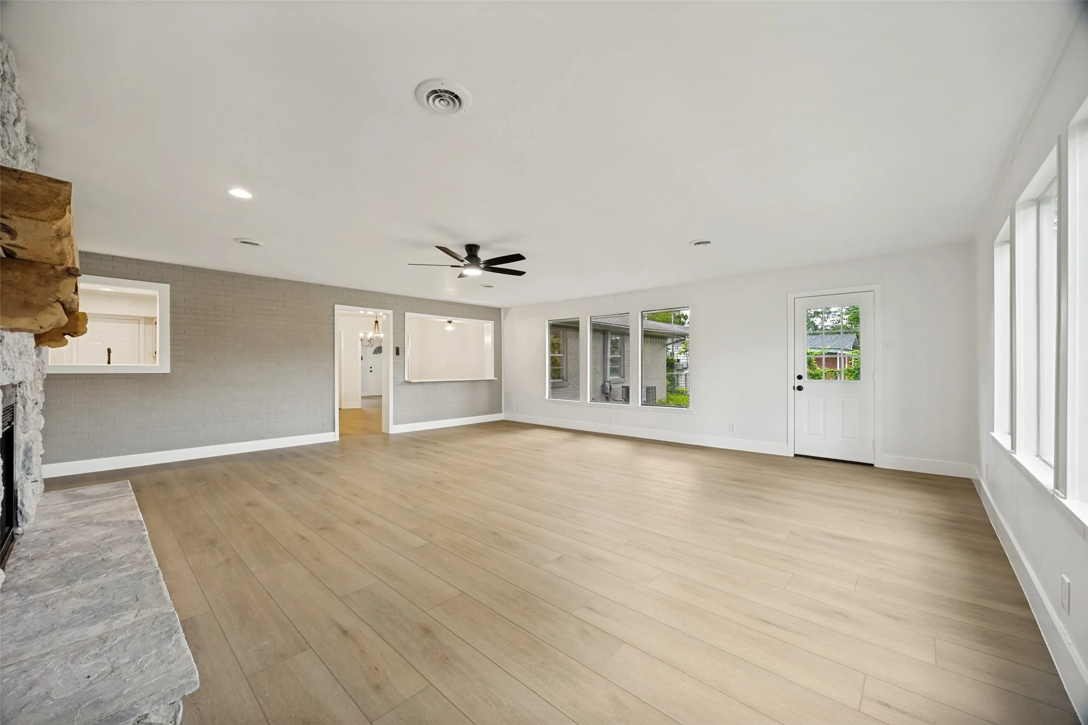 Spacious living area featuring light wood-finish flooring, a stone fireplace, recessed lighting, and multiple windows