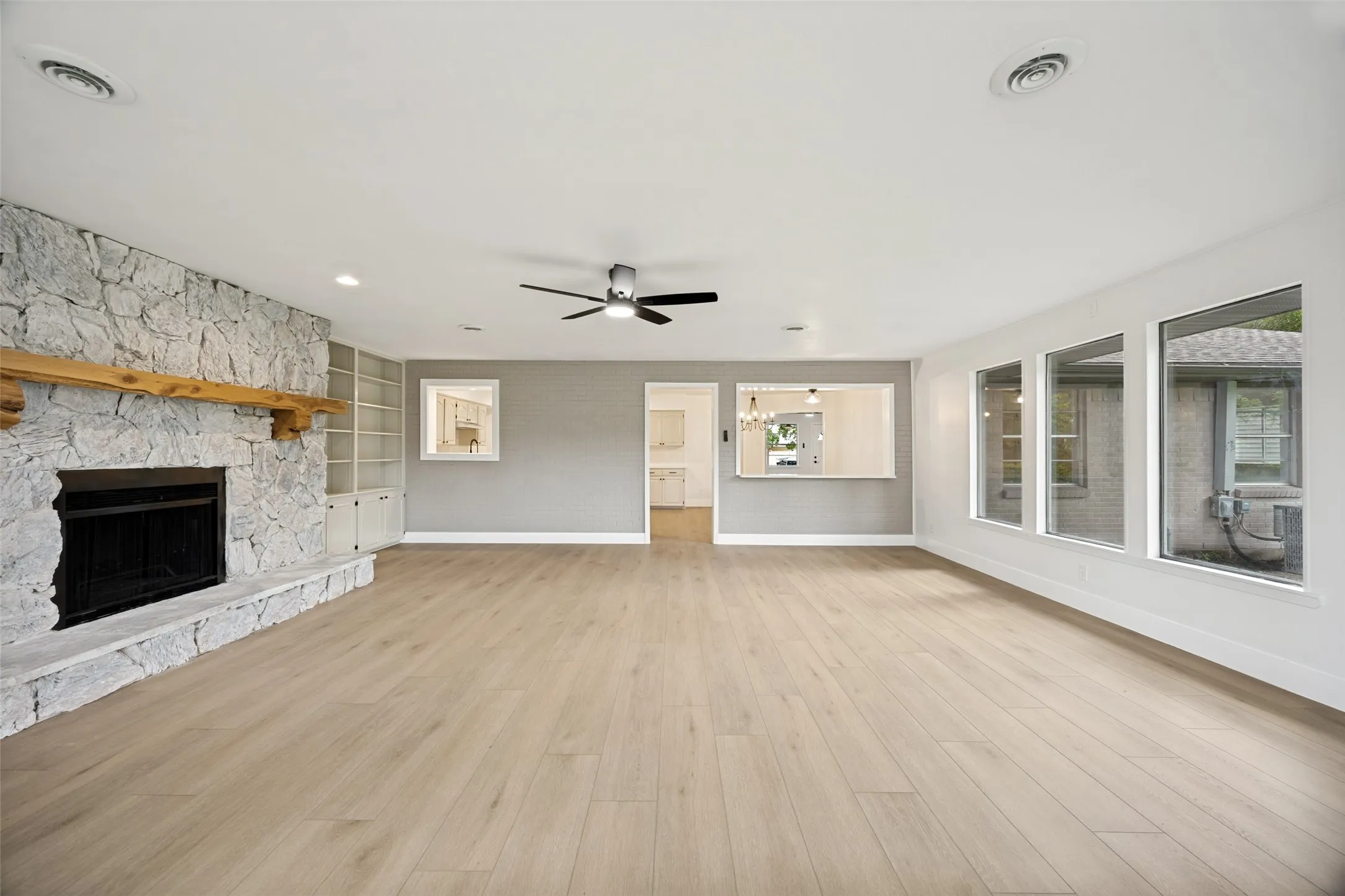 Spacious living area featuring light wood-finish flooring and a stone fireplace with a substantial wood mantel
