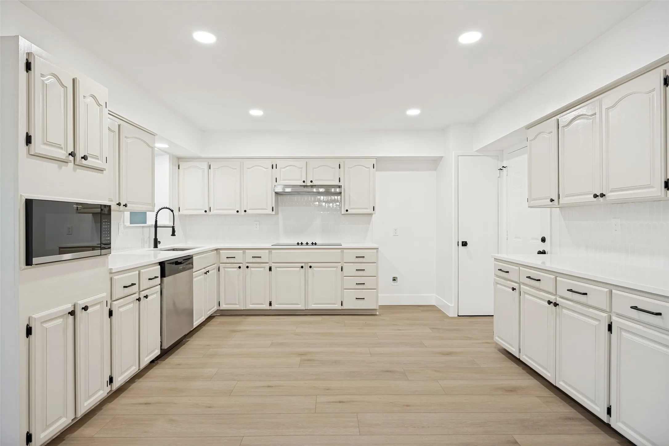 Spacious kitchen featuring extensive white cabinetry, white countertops, stainless steel appliances, wood-finish flooring, and recessed lighting