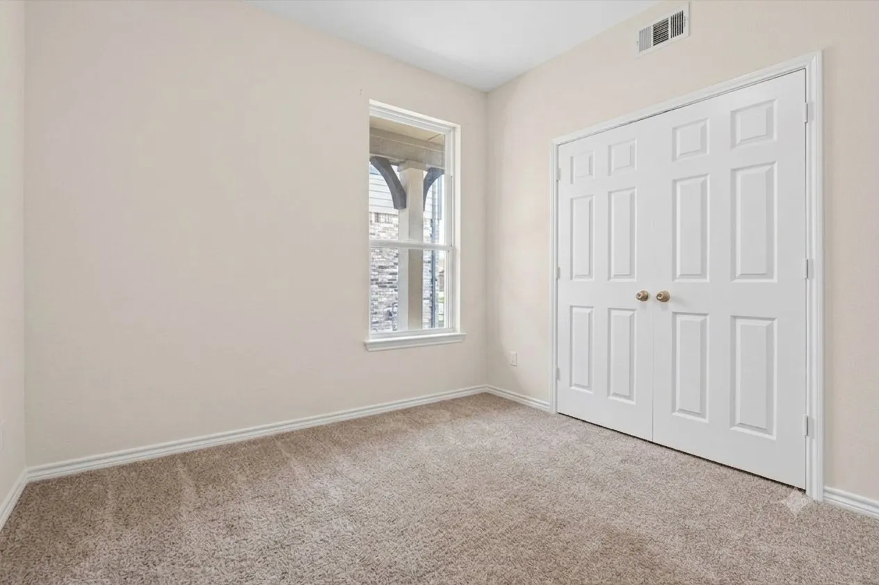 Neutral tone wall paint, carpet flooring, baseboard trim, white window frame, and bi-fold closet doors with brass hardware