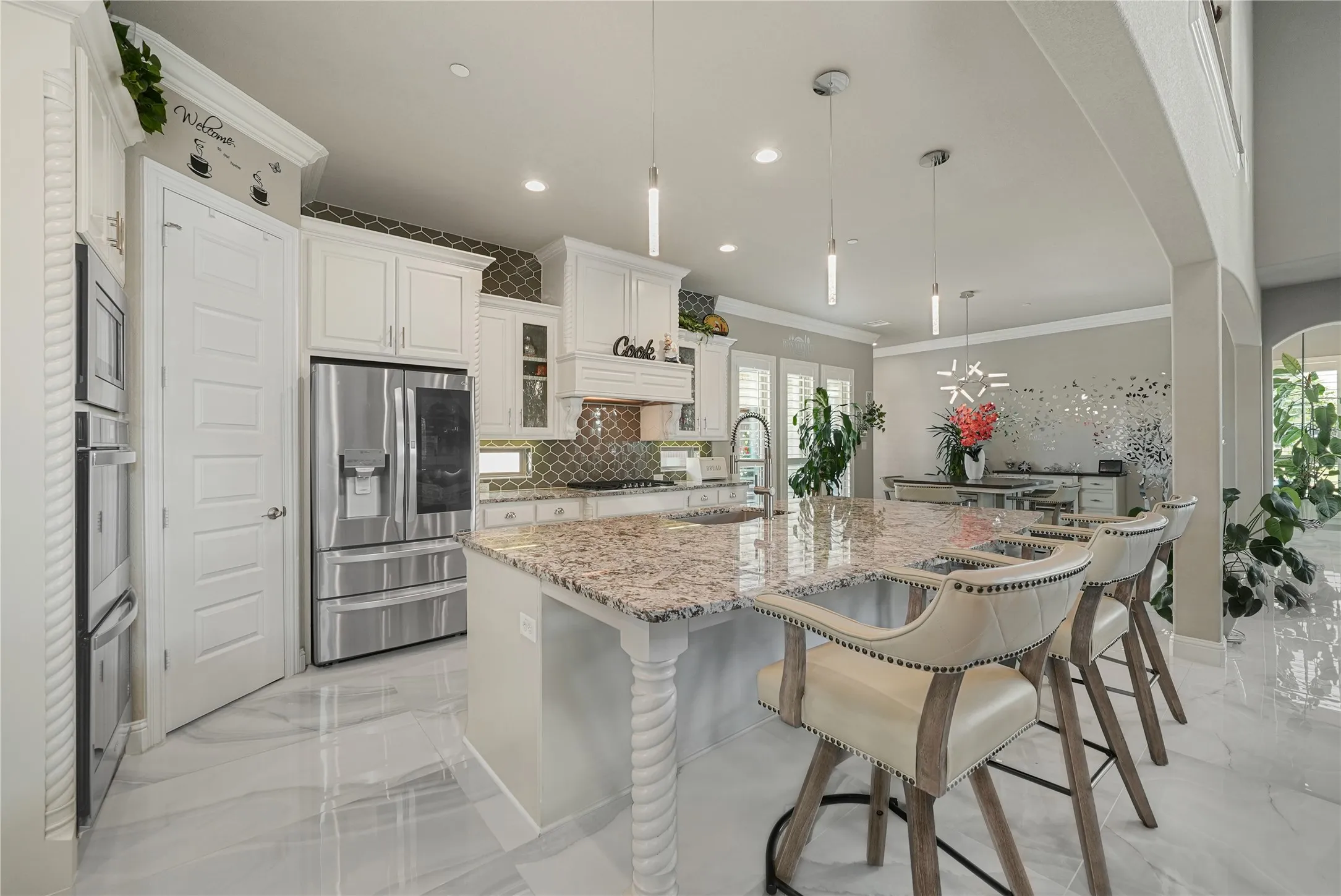 Expansive kitchen island featuring a granite countertop, white cabinetry, integrated stainless steel appliances, a decorative tile backsplash, and polished tile flooring