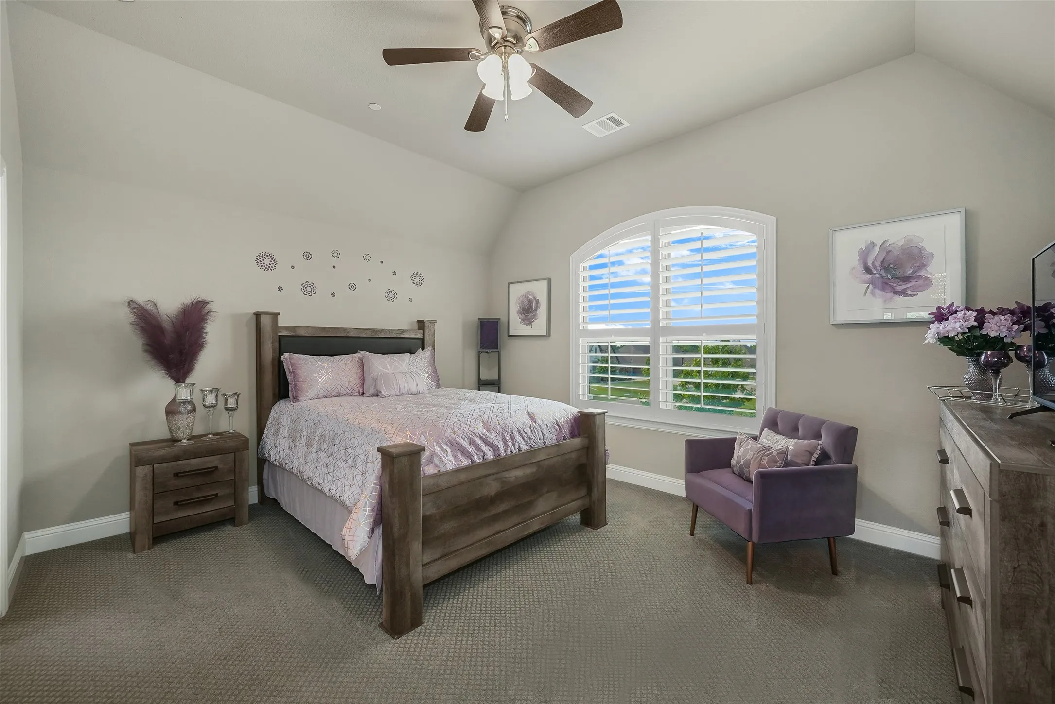 Vaulted ceiling bedroom featuring an arched window with plantation shutters, ceiling fan, and carpeted flooring