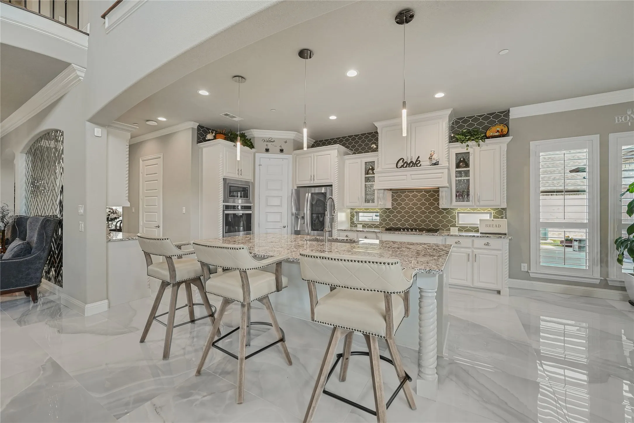 Spacious kitchen featuring an oversized island with countertop seating, white cabinetry, integrated stainless steel appliances, a decorative tile backsplash, and polished flooring