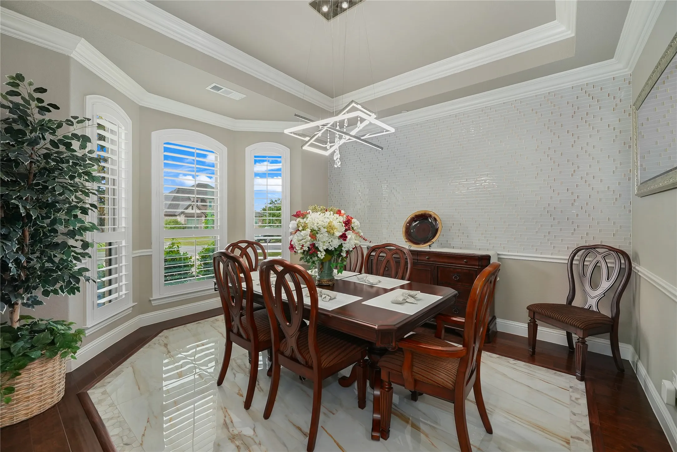 Dining area featuring a contemporary chandelier, tray ceiling with crown molding, and a decorative accent wall