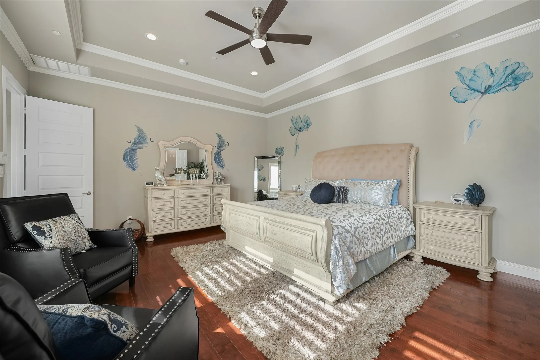 Spacious bedroom featuring wood-finish flooring, a tiered tray ceiling with recessed lighting, and a ceiling fan