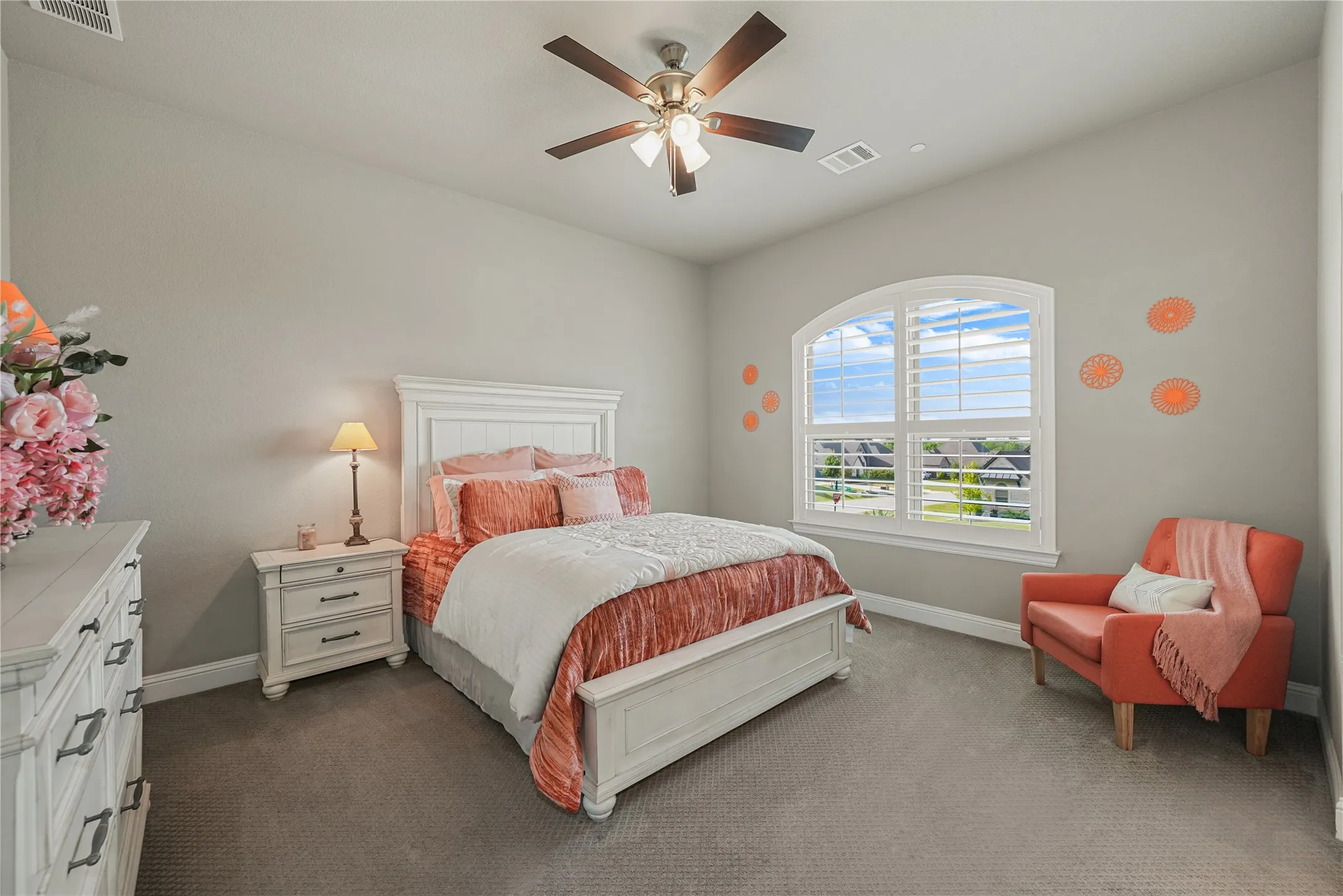 Bedroom featuring an arched window with louvered shutters, ceiling fan with integrated lighting, textured carpeting, and light-toned wall paint