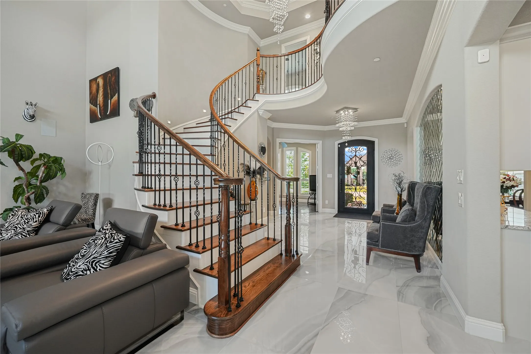Grand foyer featuring a curved staircase with wrought iron balusters and wood handrails, high ceilings, polished tile flooring, and an ornate front entry door with glass inserts
