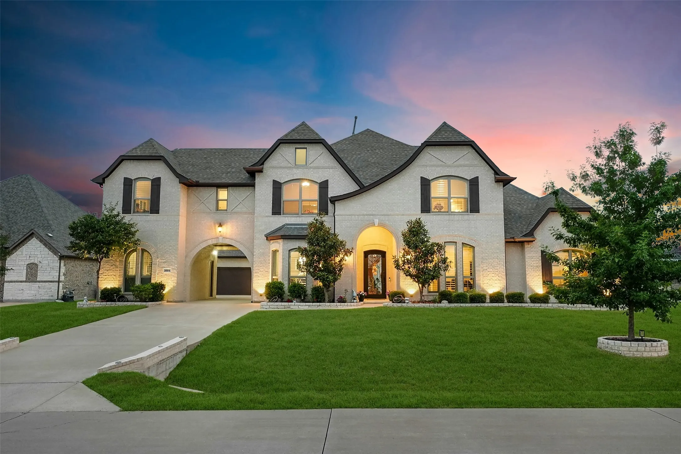 Architectural residence featuring a light-colored brick facade, dark roofing, and decorative shutters