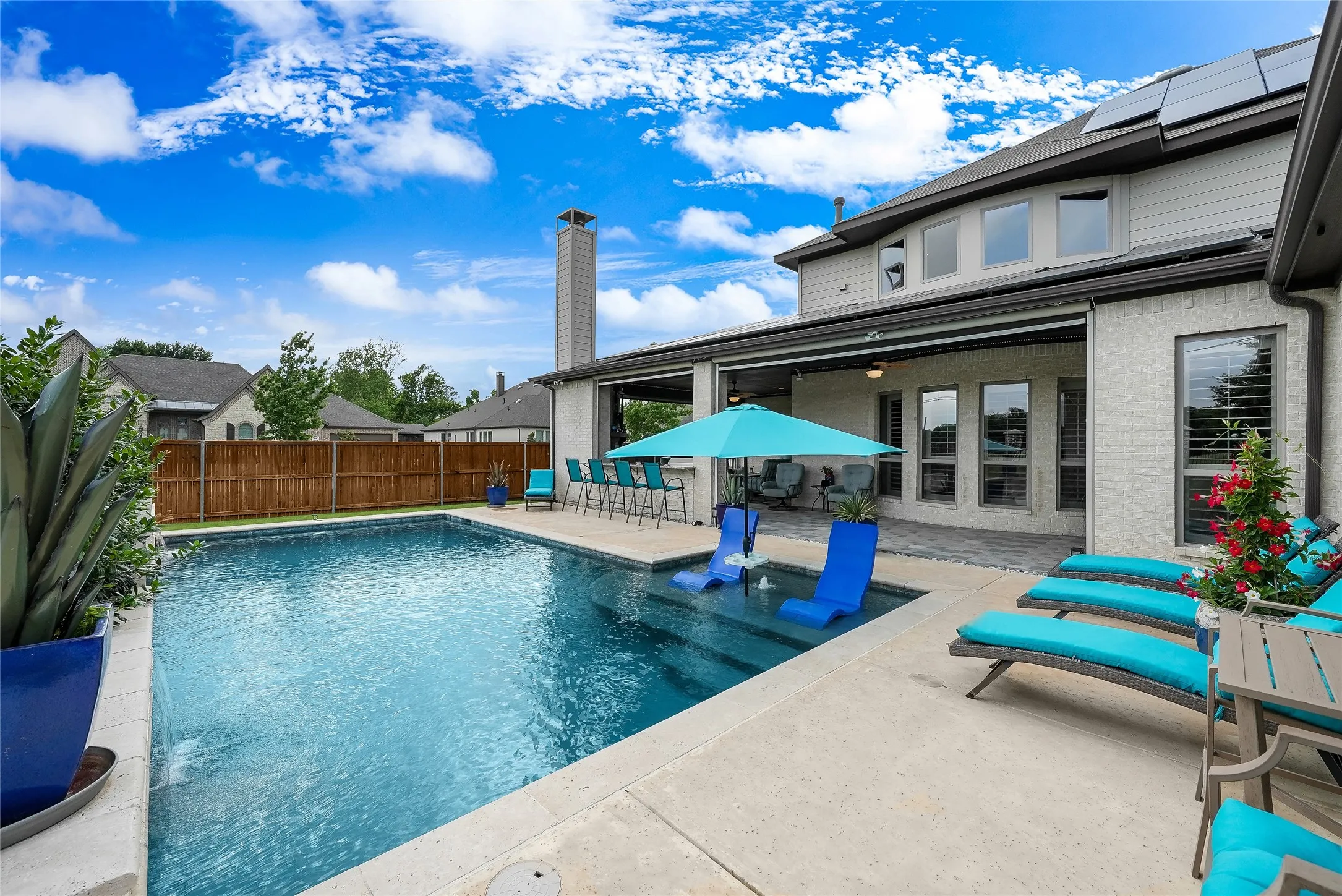 Private backyard featuring a rectangular swimming pool with integrated tanning ledge, a stone patio, and a covered outdoor living area