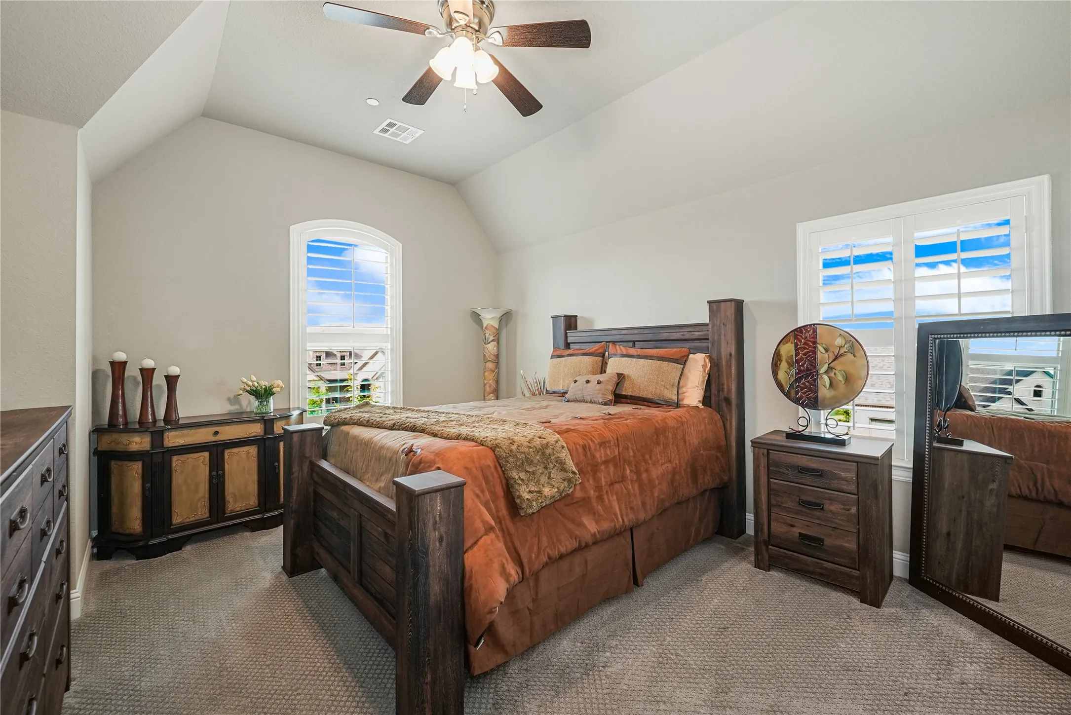 Vaulted ceiling room featuring two windows with plantation shutters, a ceiling fan with integrated lighting, and neutral-toned carpeting