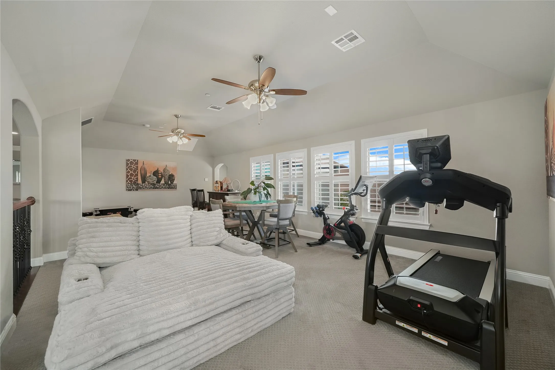Spacious bonus room featuring vaulted ceilings, multiple windows with plantation shutters, ceiling fans, and carpeted flooring