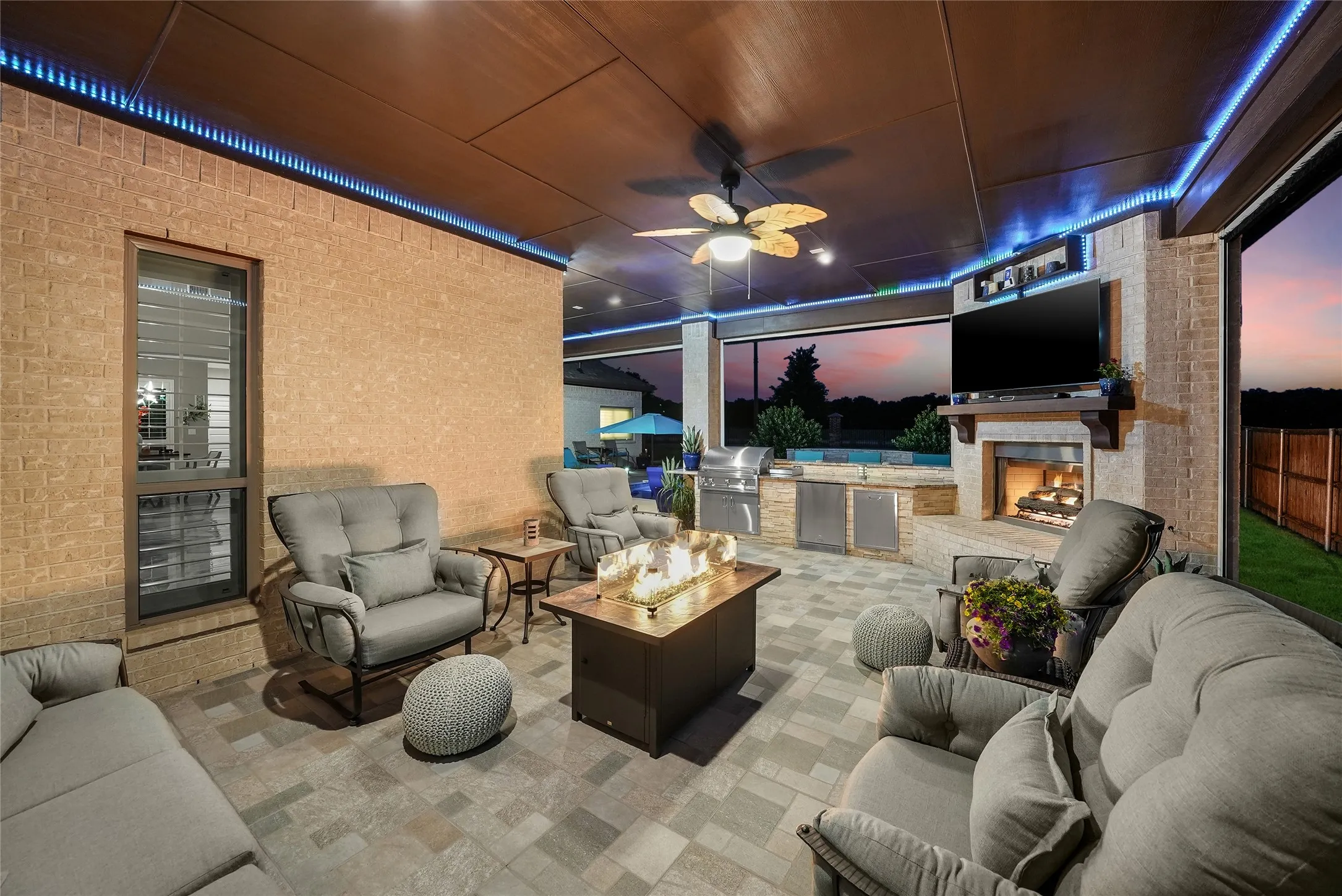 Covered outdoor patio featuring a built-in outdoor kitchen, a stone-clad fireplace with a mantle, and integrated ceiling lighting