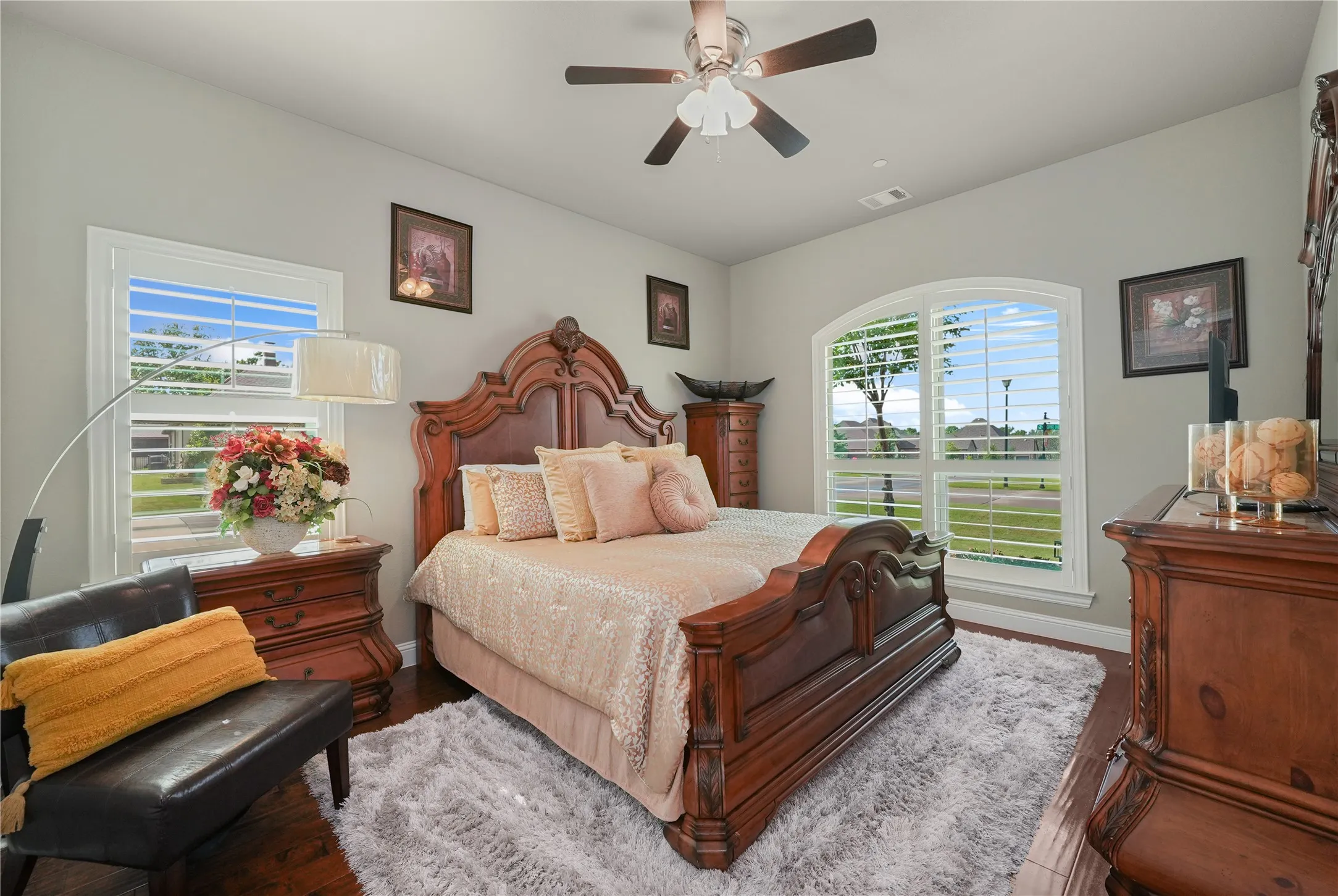 Bedroom featuring wood-finish flooring, a ceiling fan, and two windows with white louvered shutters