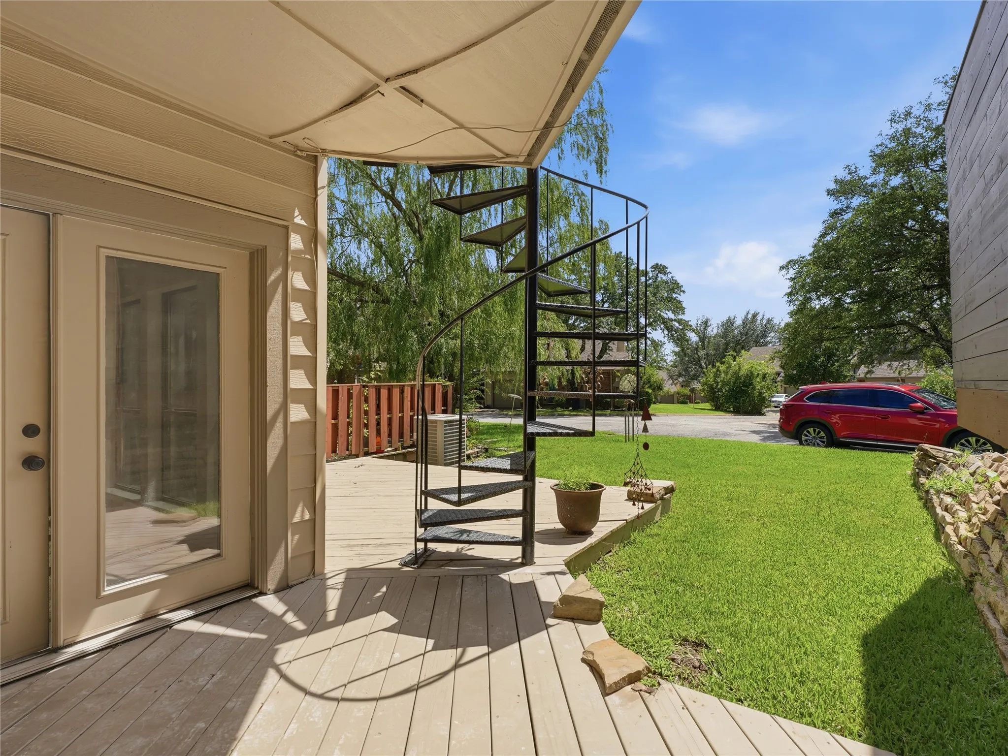 Expansive outdoor deck featuring a black spiral staircase, a glass-paneled door, siding exterior, and a grassy yard