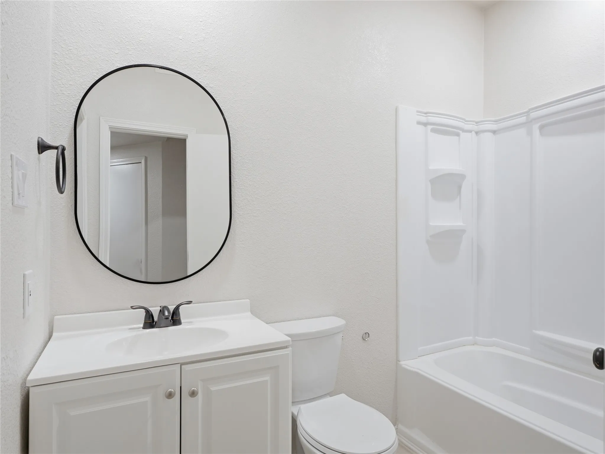 Bathroom featuring a white vanity with integrated sink, black-finish faucet, and an oval-framed mirror