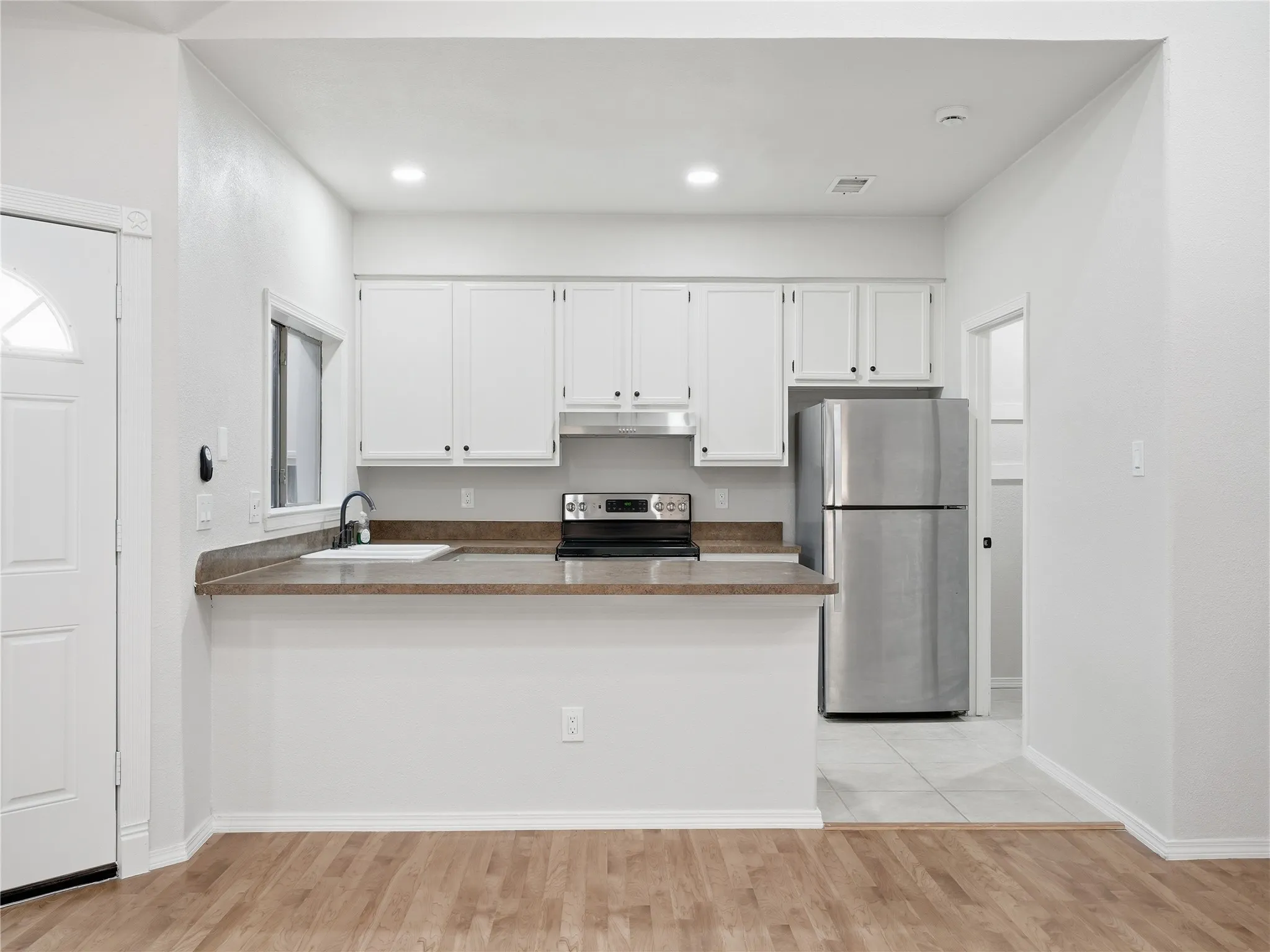 Bright kitchen featuring white cabinetry, stainless steel appliances, a breakfast bar, and wood-finish flooring