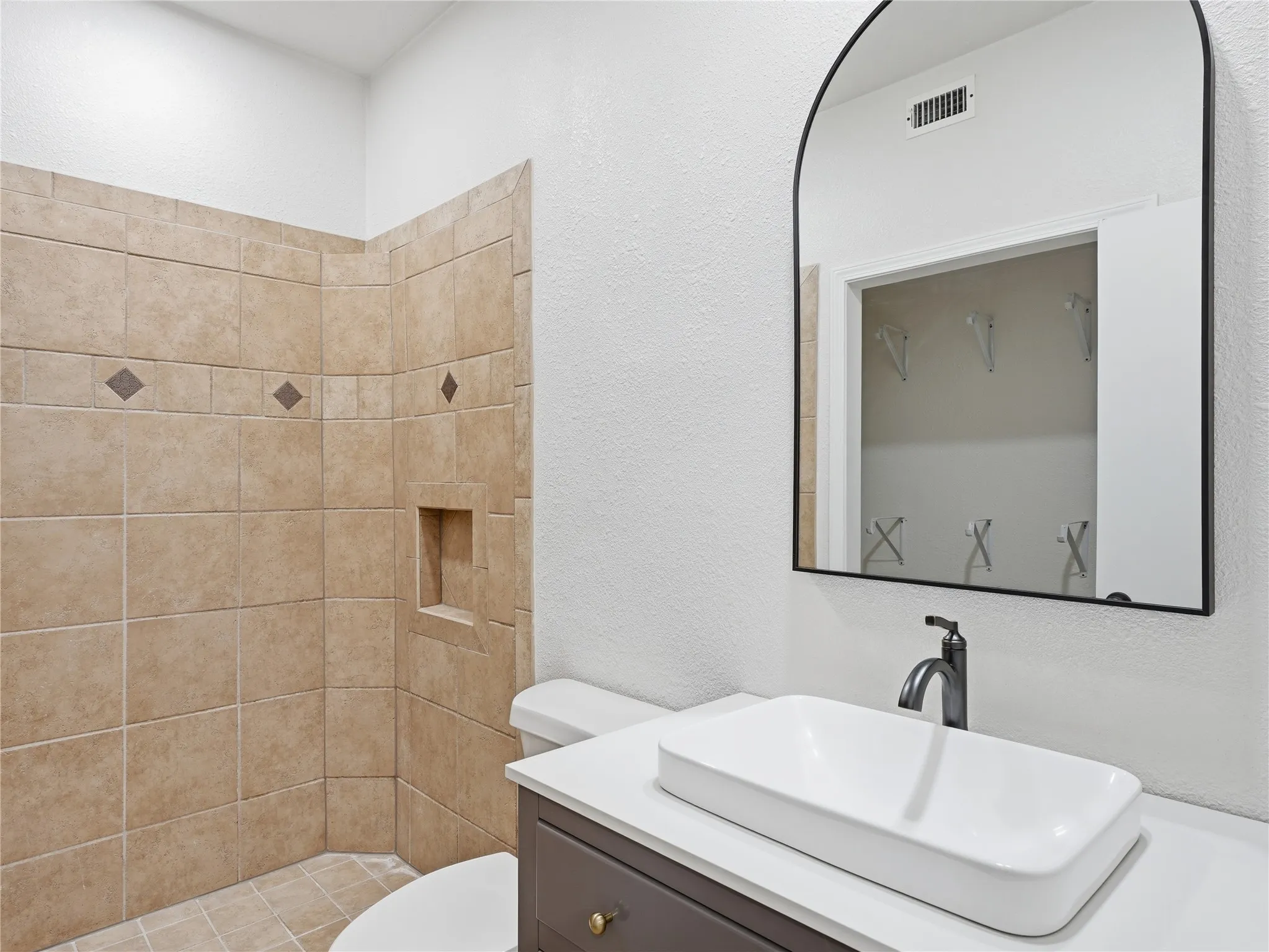 Contemporary bathroom featuring a vessel sink, dark-finish faucet, and a black-framed arched mirror