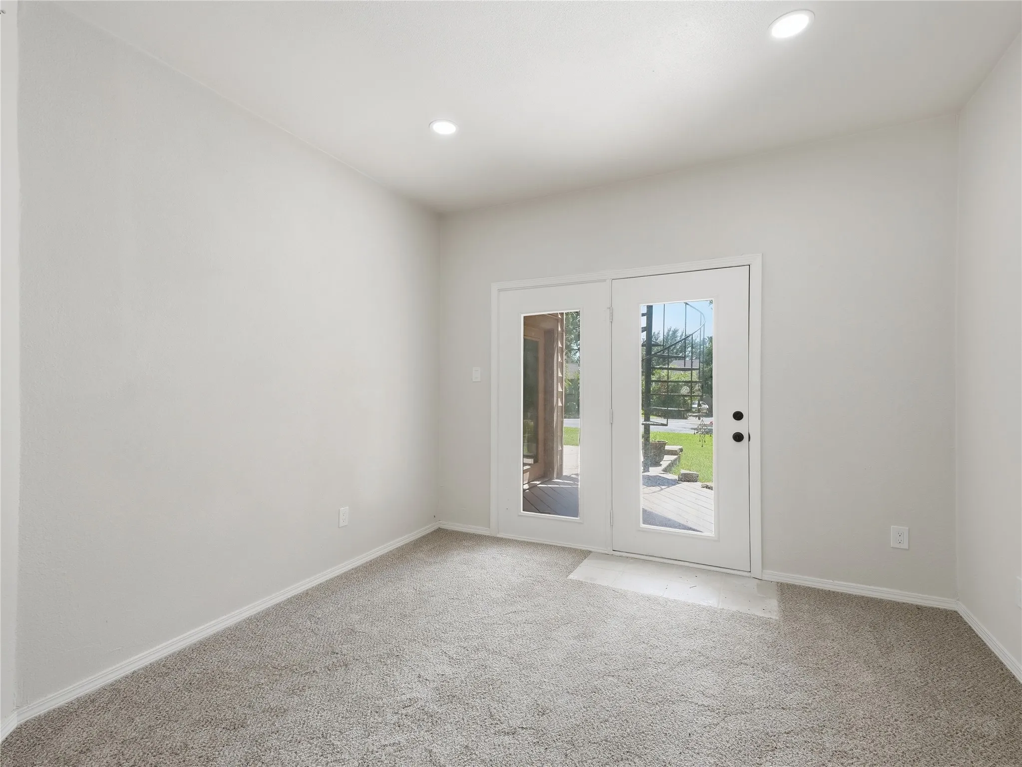 Room featuring light gray carpet, white walls, recessed lighting, and white French doors with glass panes opening to an outdoor patio with wood decking