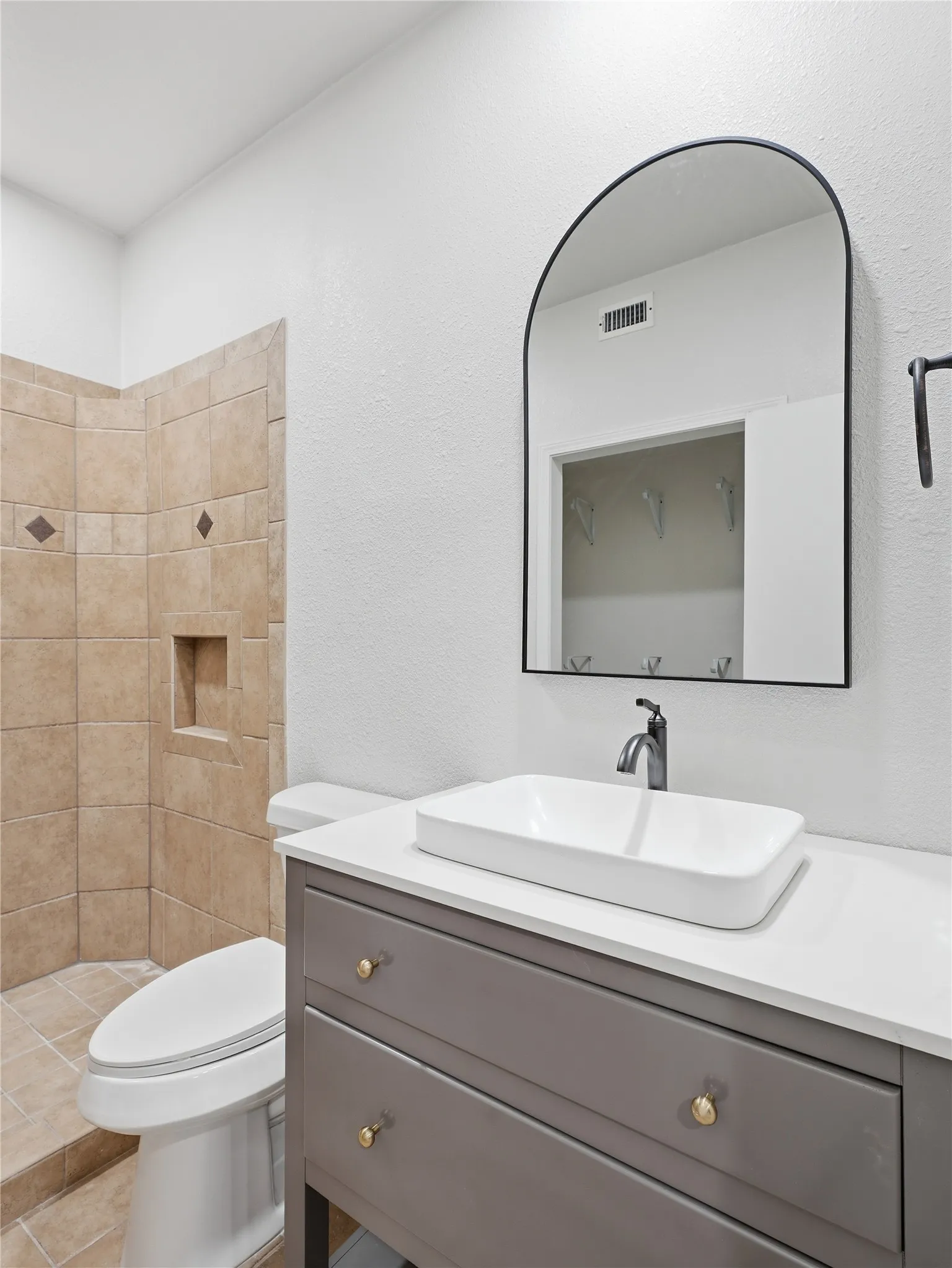Bathroom featuring a vessel sink, quartz-finish countertop, gray vanity with gold-tone hardware, and an arched wall mirror
