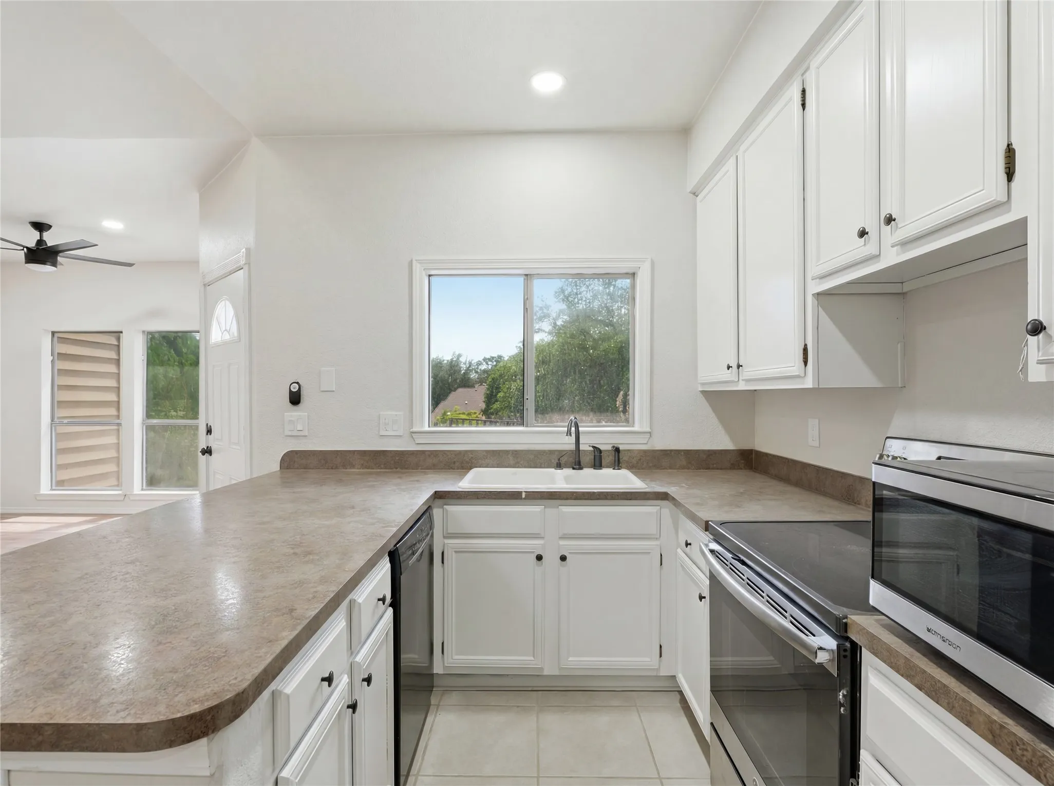 U-shaped kitchen featuring white cabinetry with dark hardware, a white sink, and light-colored​​‌​​​​‌​​‌‌​‌‌​​​‌‌​‌​‌​‌​​​‌​​ countertops