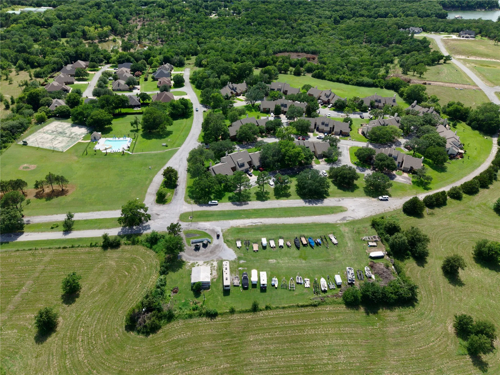 Aerial overview of a residential community featuring multiple homes with dark roofing, a communal swimming pool, and a tennis court