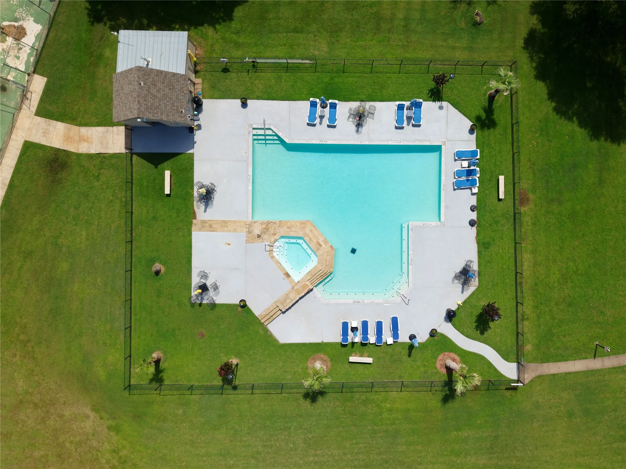 Fenced swimming pool area featuring a built-in spa, concrete decking, and a separate pool house with a shingled roof