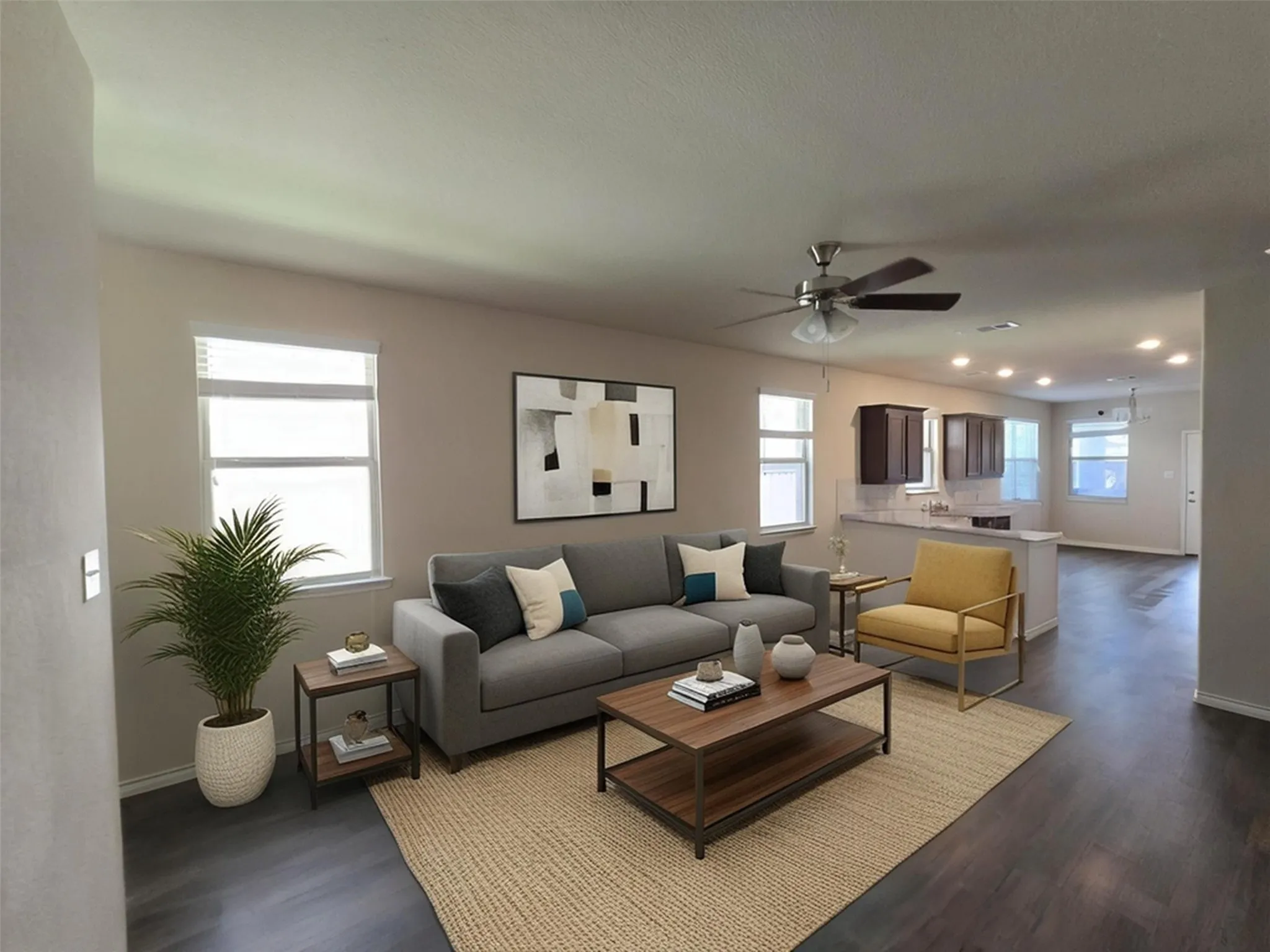 Open-concept living space featuring expansive wood-finish flooring, multiple windows, a ceiling fan, recessed lighting, and a partial view of the kitchen with dark wood cabinetry and a light-toned countertop
