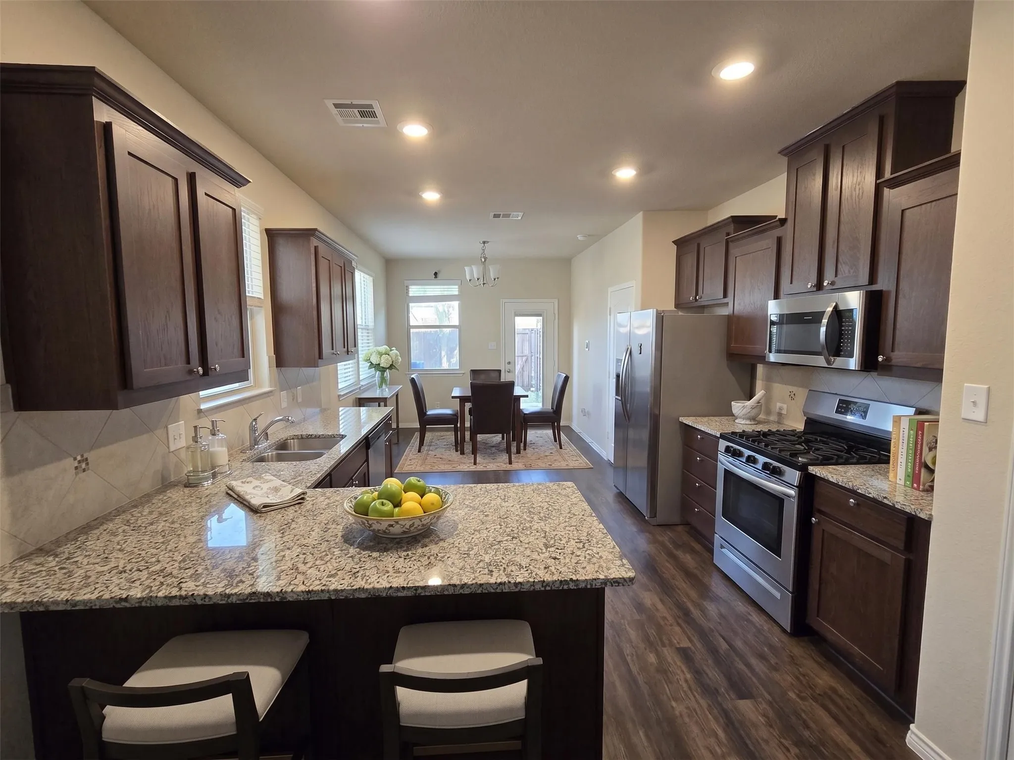 Open-concept kitchen featuring wood-finish flooring, dark wood cabinetry, and granite countertops