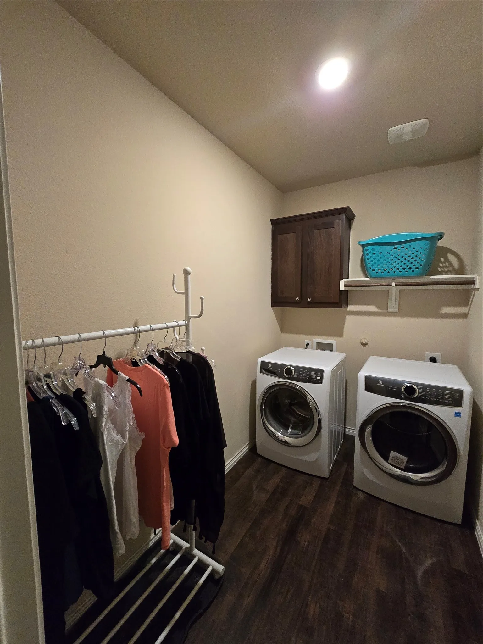 Dedicated laundry area featuring wood-finish flooring, a wall-mounted dark wood cabinet, and an overhead storage shelf