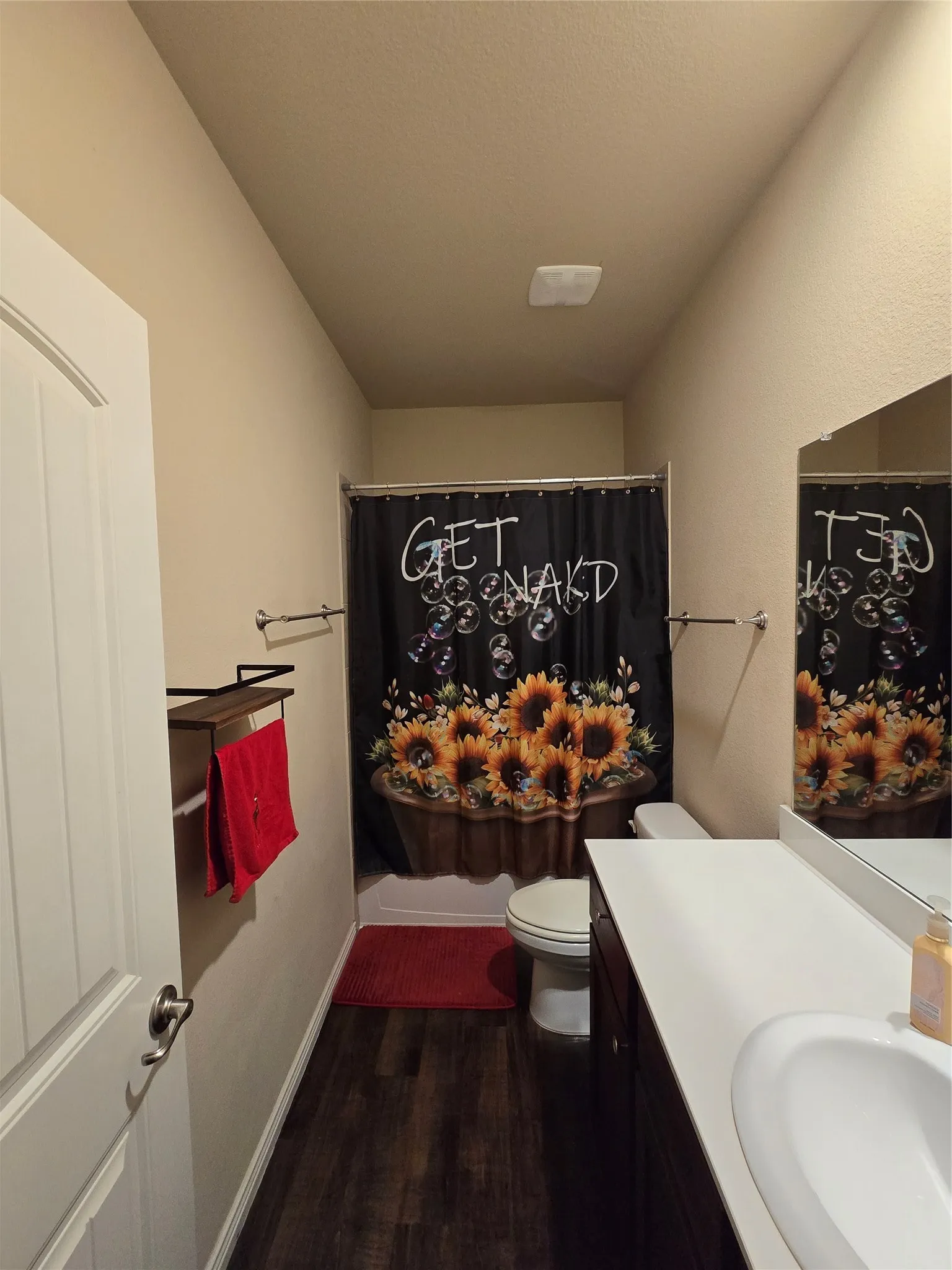 Bathroom featuring dark wood-finish flooring, a white vanity with an integrated sink, a large wall mirror, a toilet, and a white bathtub